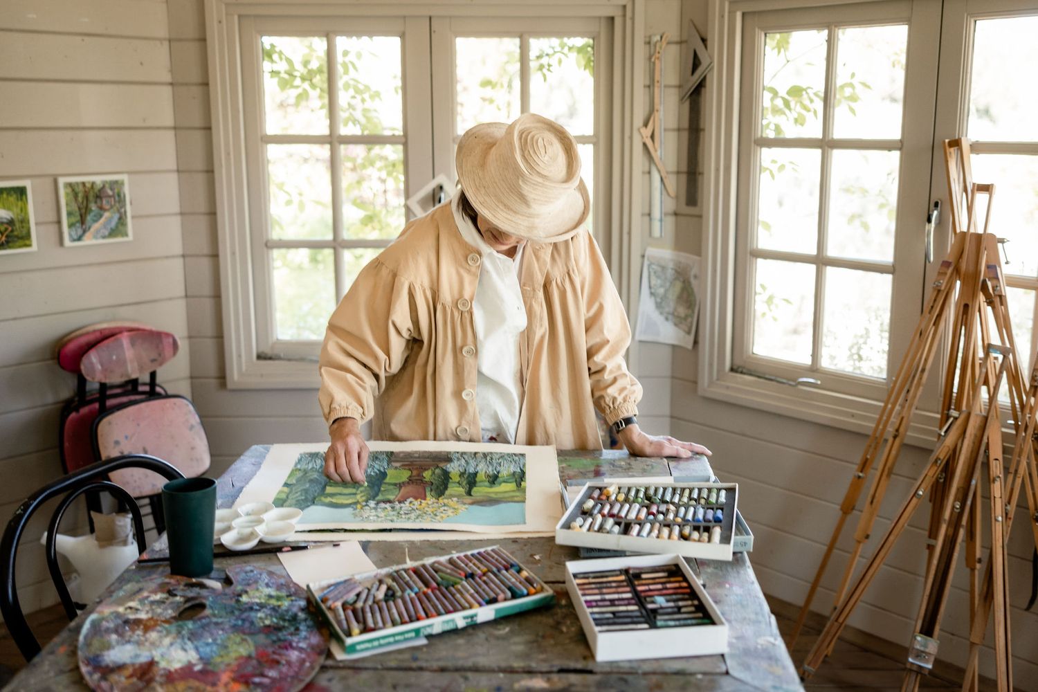 Artist studio interior with wooden easels, natural light from windows, and painting supplies in a rustic room.