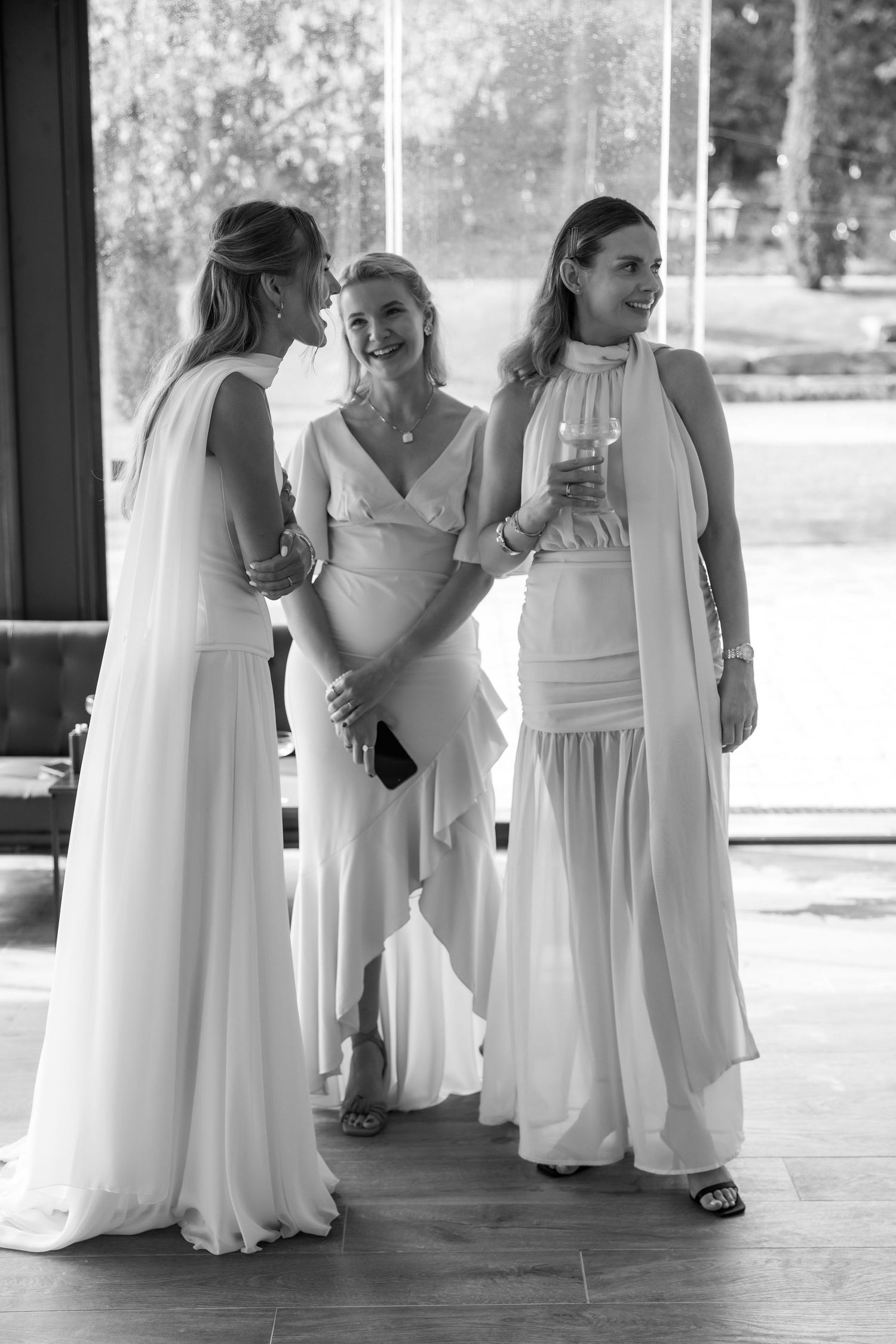 A group in flowing white dresses gather together on a light-colored floor in what appears to be a wedding party.