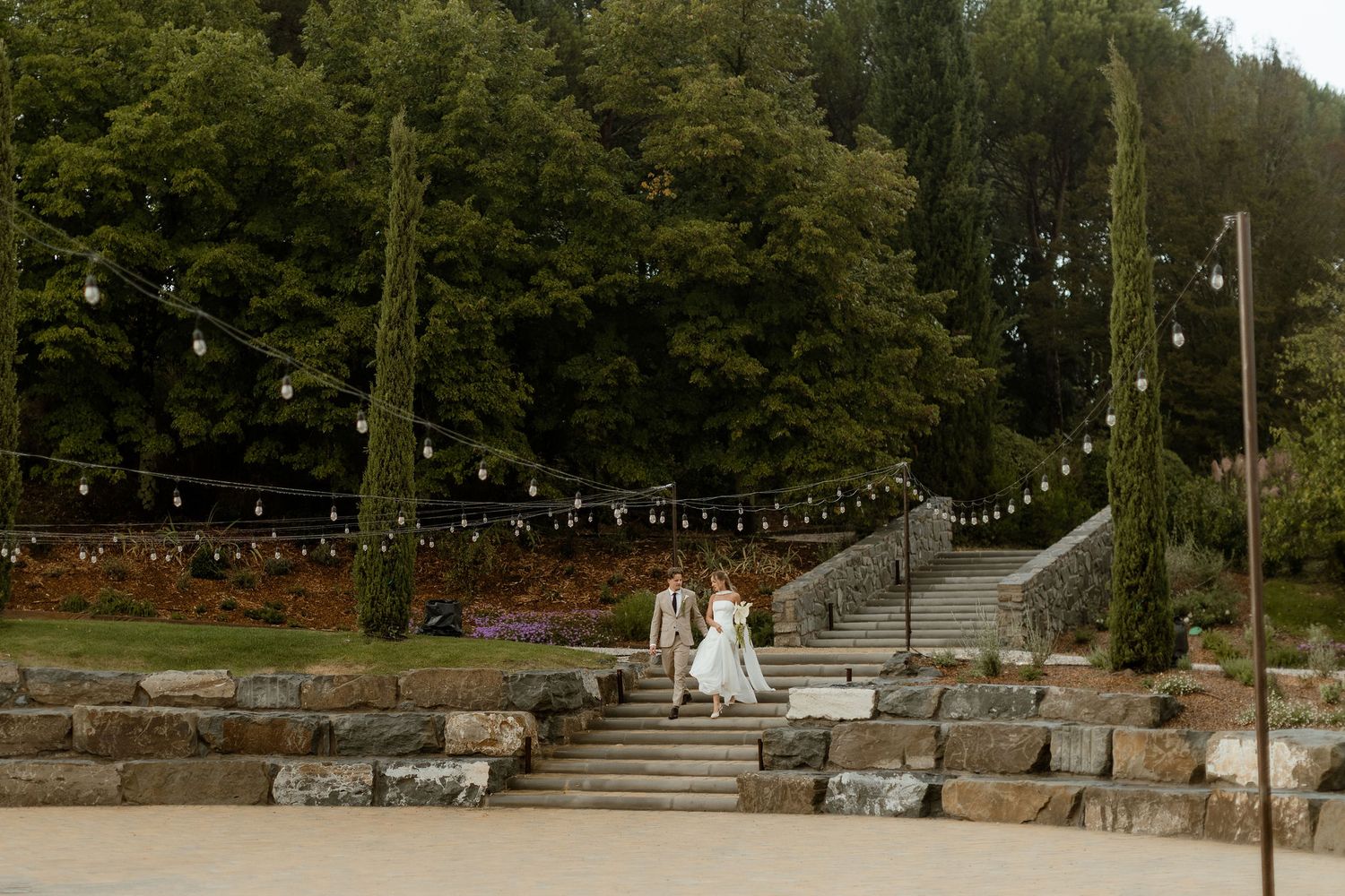 A stone staircase with string lights leads up a wooded hillside at an outdoor venue.