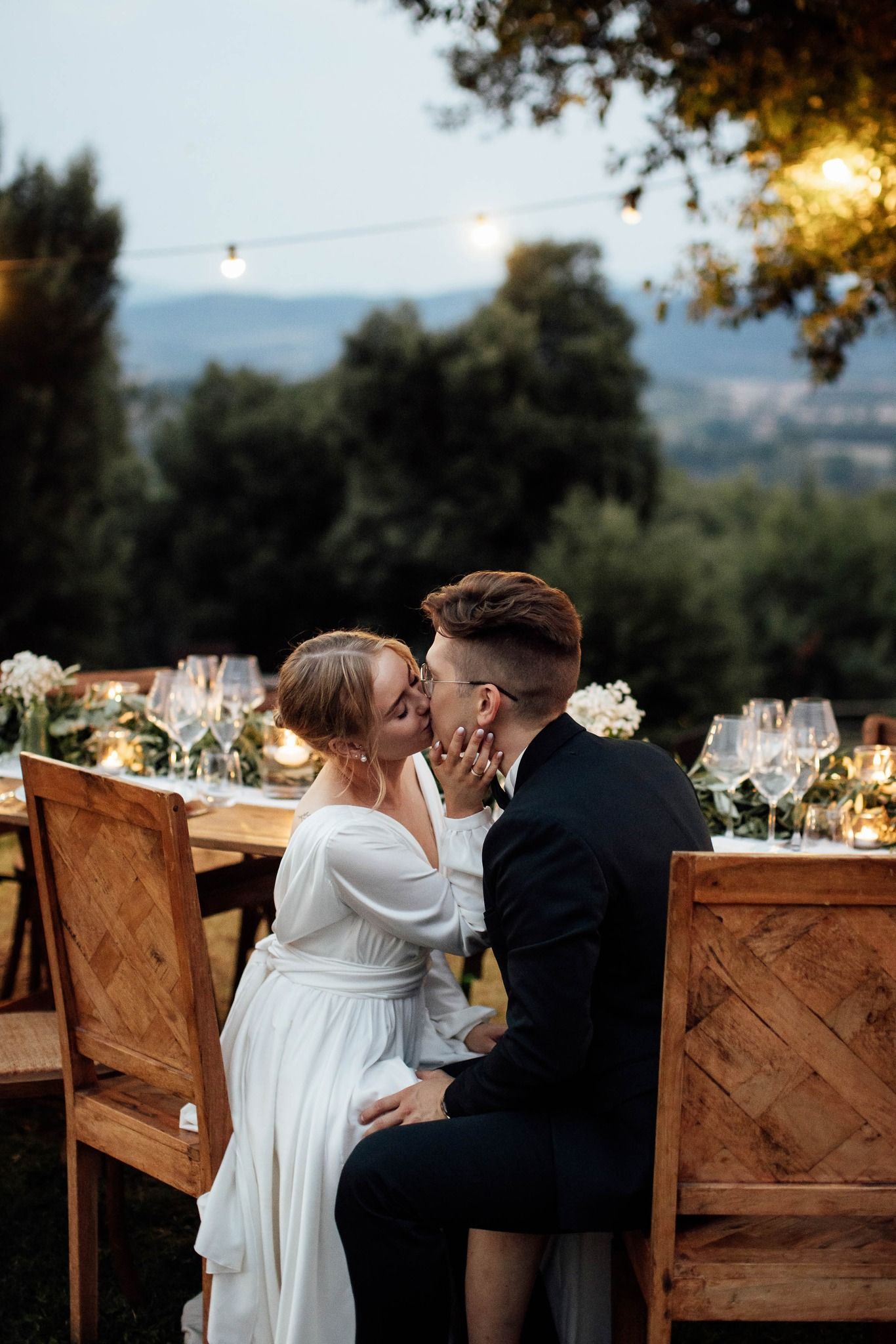 Romantic outdoor wedding reception scene with couple sharing intimate moments at wooden tables during golden hour.
