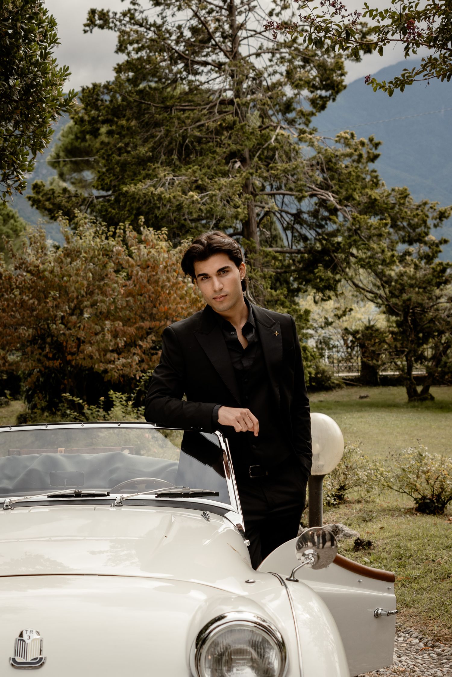 Sophisticated fashion shoot featuring classic white Triumph car in garden setting.