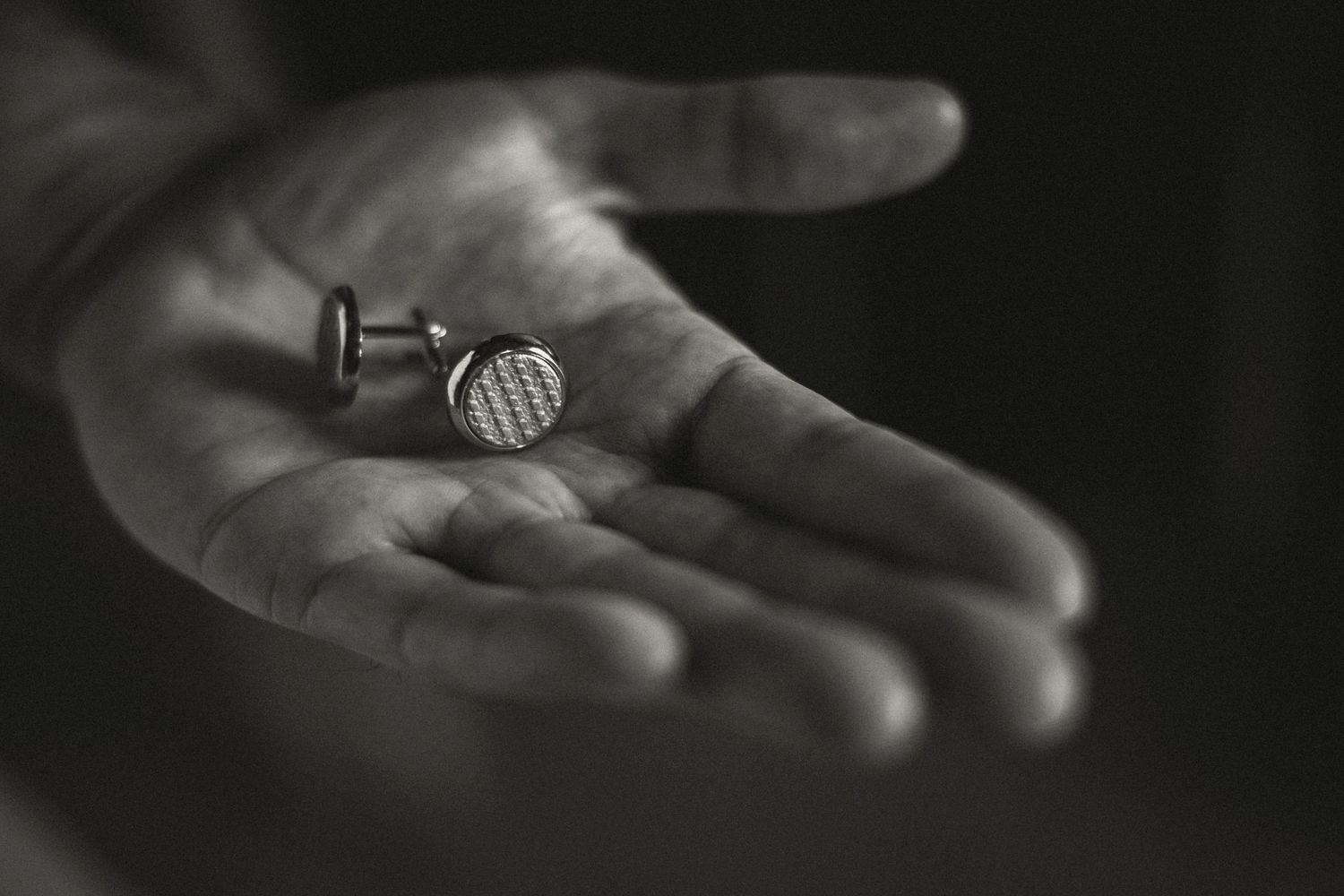 Black and white close-up of wedding cufflinks held in open palm.