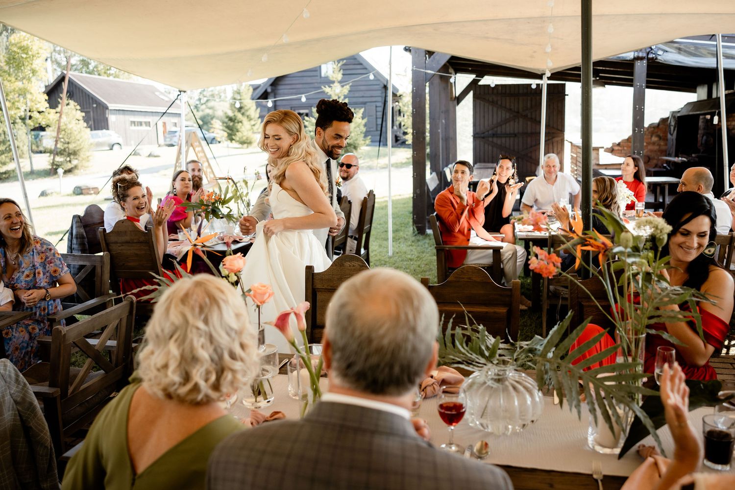 Wedding guests under a tent raise their glasses during a celebratory toast.