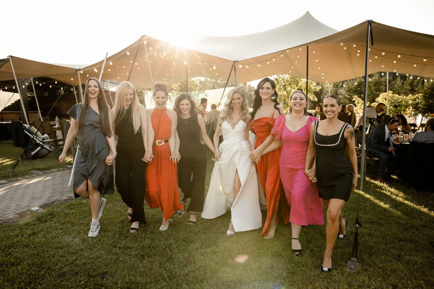 Wedding group walks together under outdoor tent at sunset celebration.