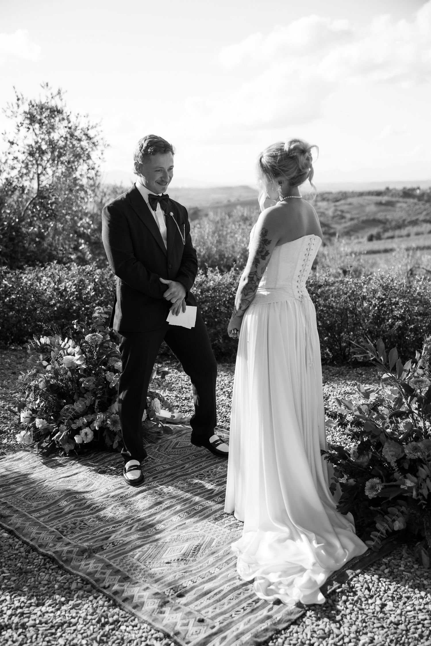 Black and white wedding photo showing couple standing on a garden path during an outdoor ceremony.