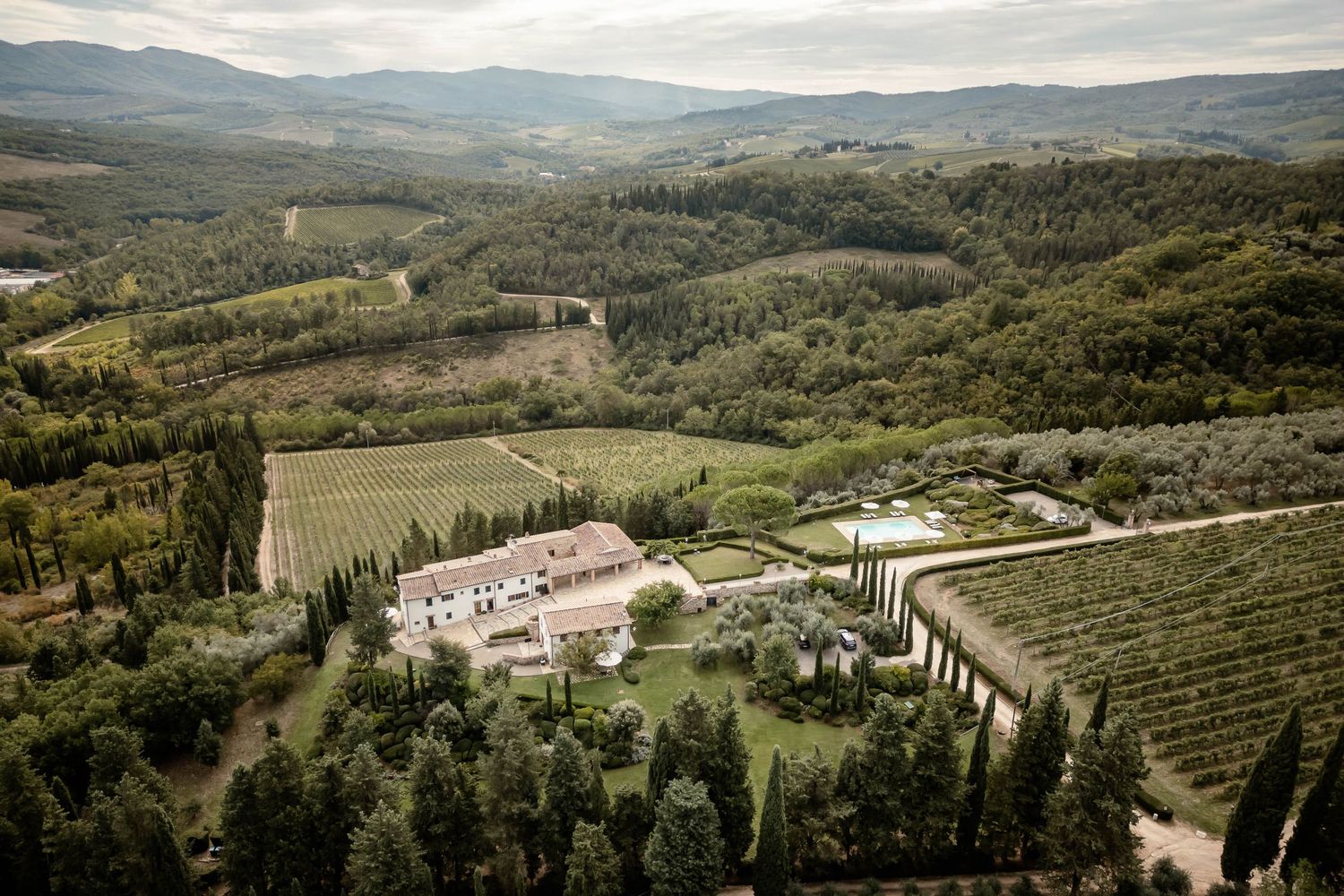 Aerial view of Tuscan villa estate surrounded by rolling hills and cypress trees.