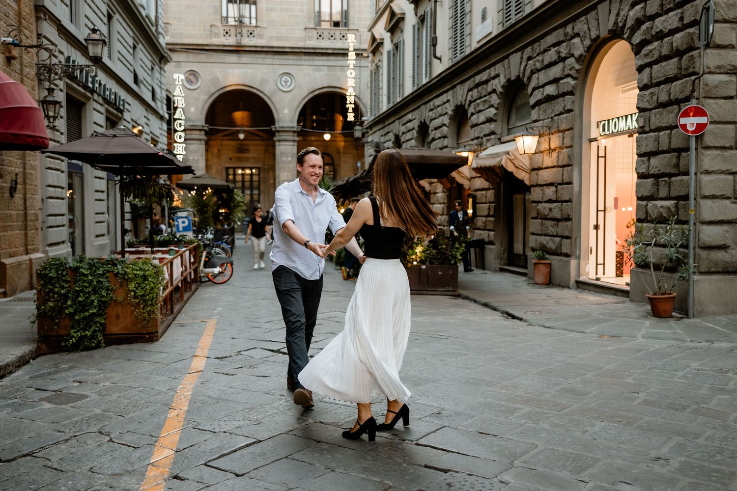 A couple dancing together on a charming cobblestone street in Florence with historic architecture and shops in the background.