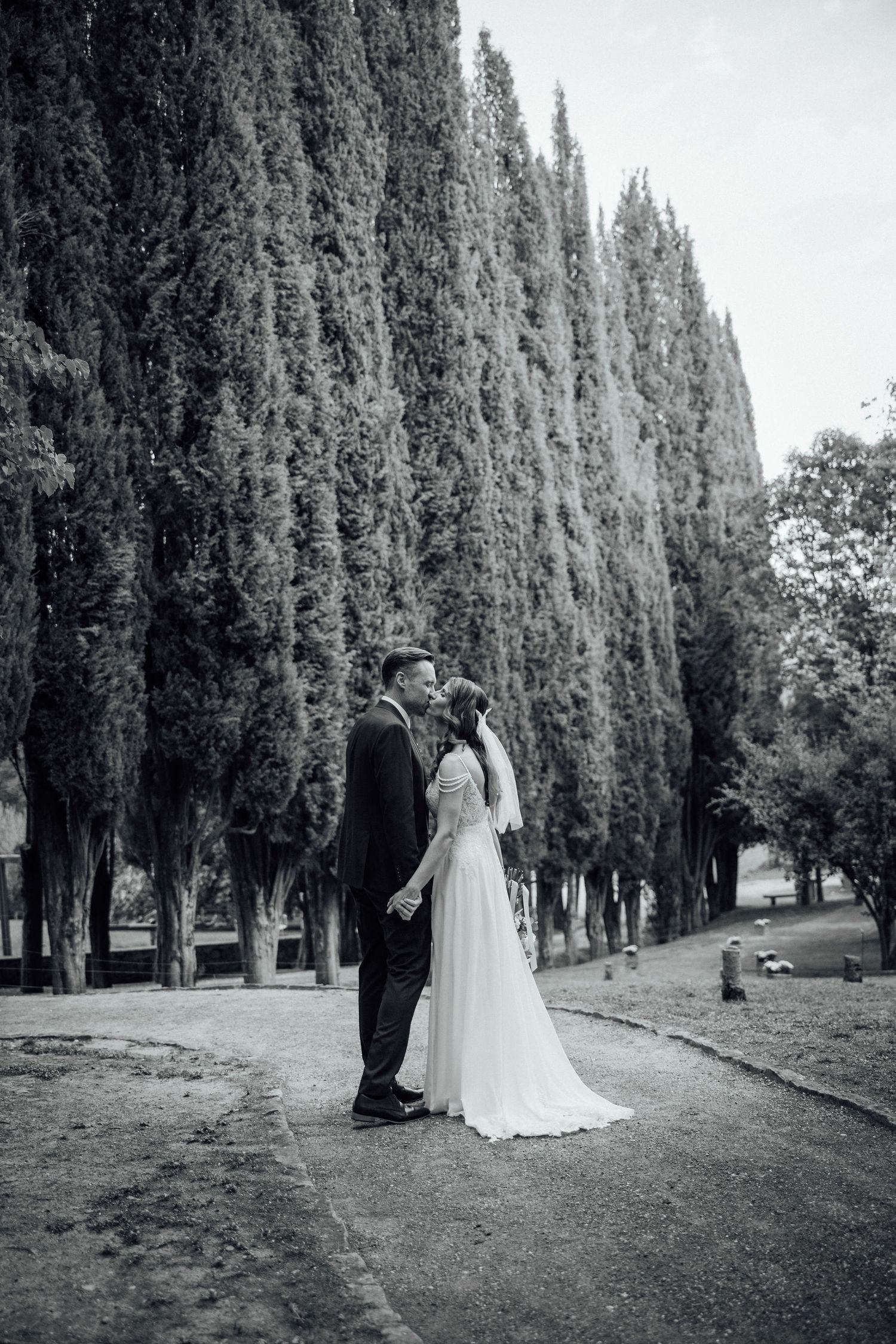 A wedding couple shares an intimate moment along a path lined with majestic cypress trees.