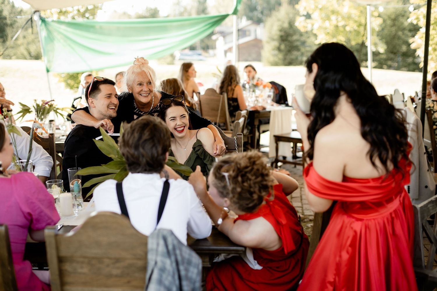 Wedding guests laugh and share a joyful moment under an outdoor tent at a reception celebration.