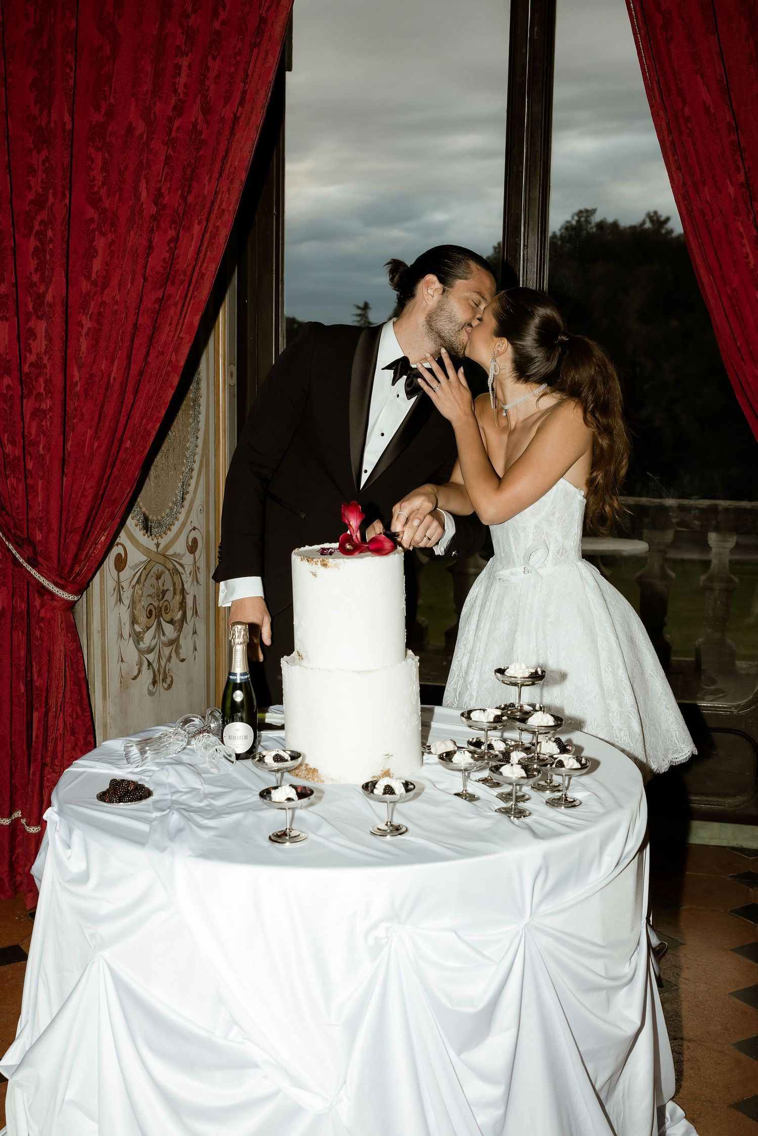 Wedding reception table with white linens and red curtains showing progression of cake cutting and romantic newlywed moment.