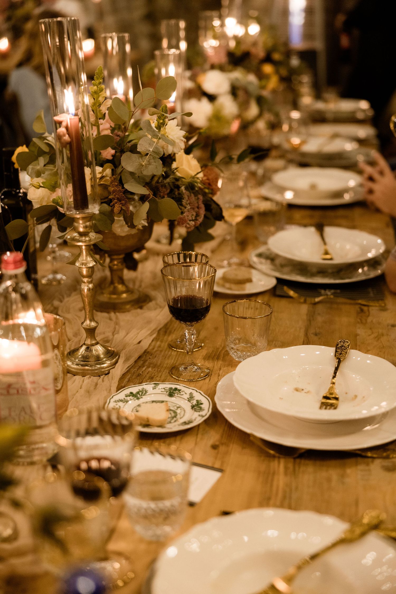 Elegant table setting with glowing candles, white plates and floral arrangements at a formal dinner party.