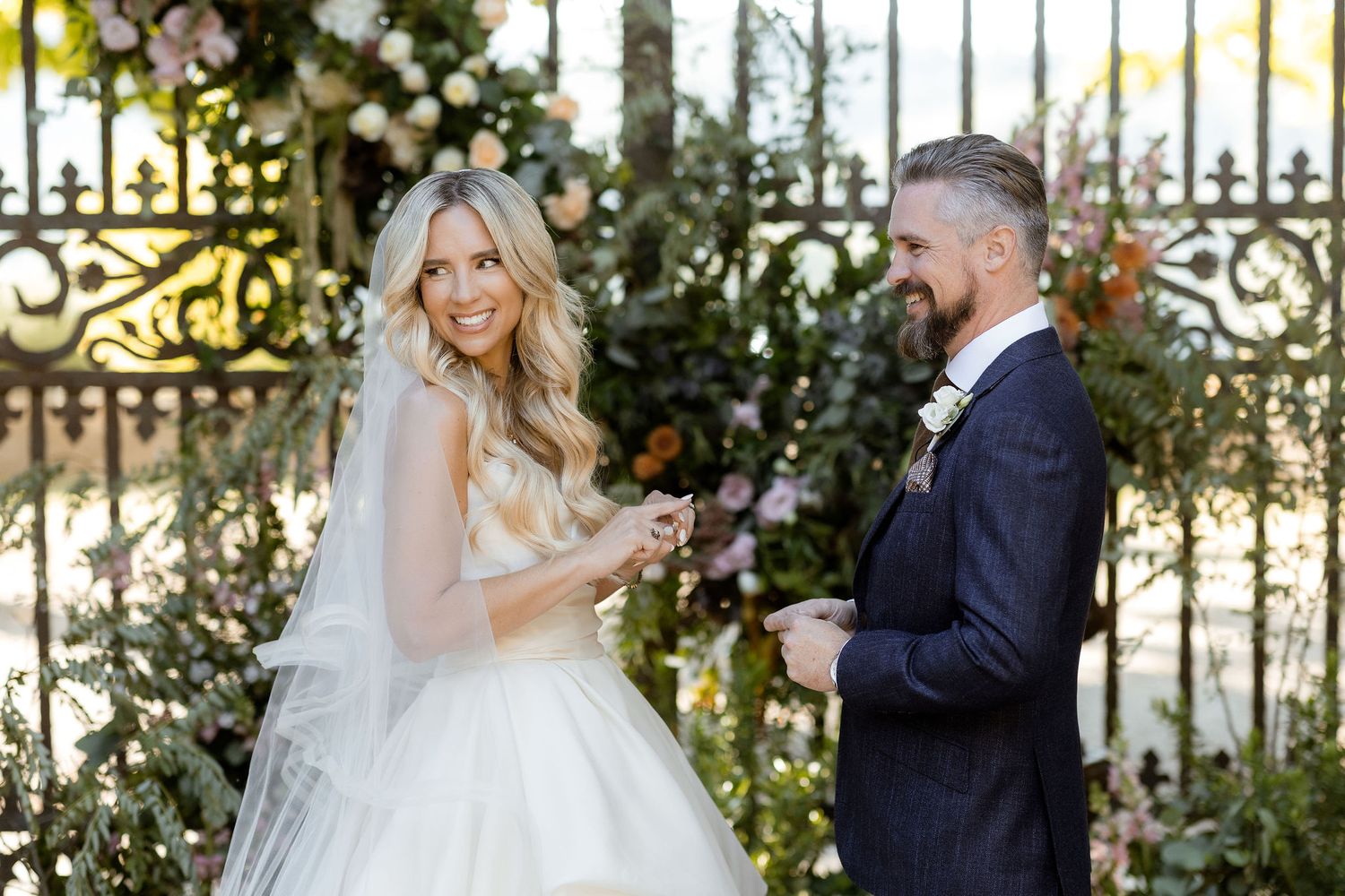 Wedding couple shares intimate moments in a garden setting with ornate iron gates and lush greenery.