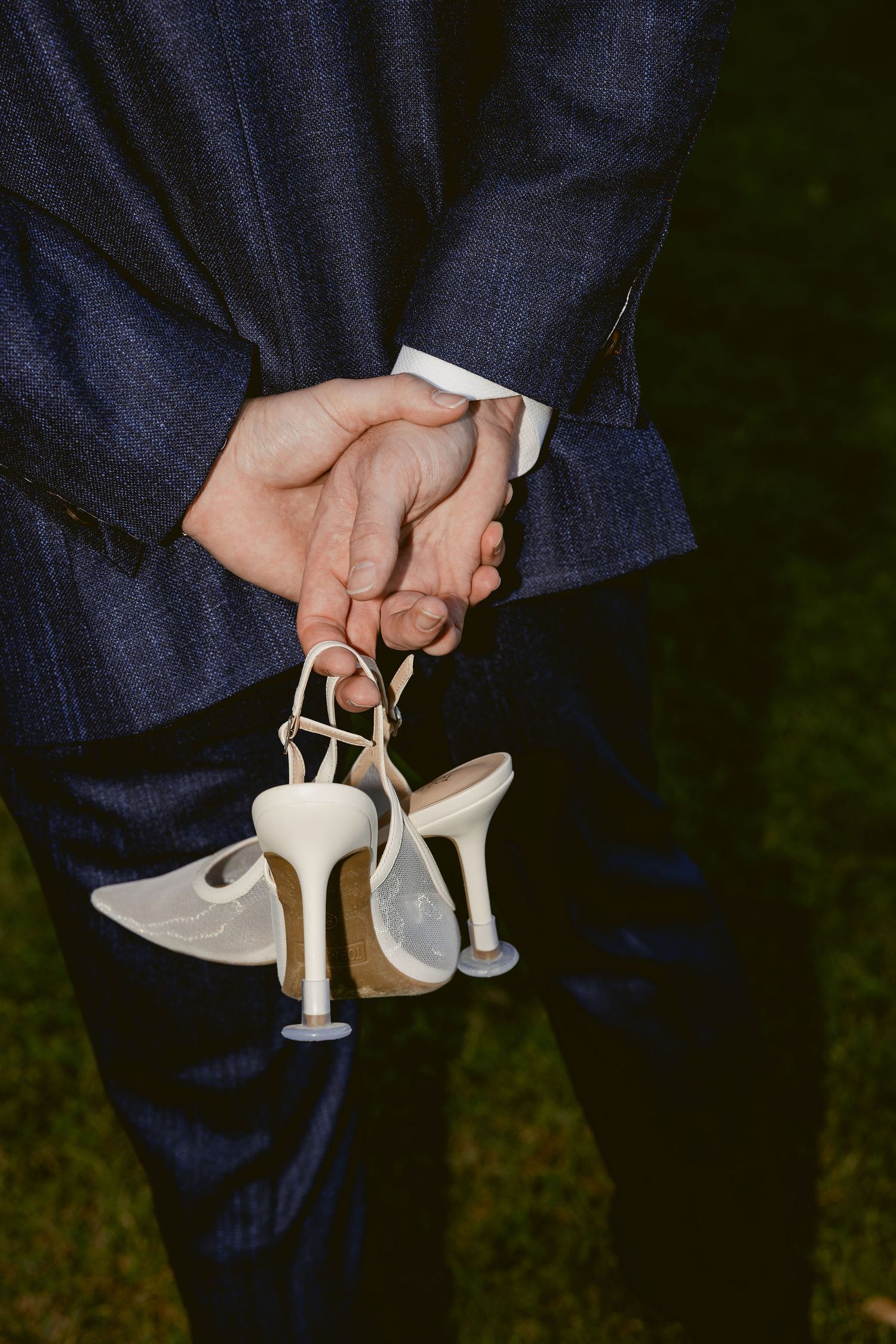 A series of close-up shots showing hands holding elegant white high-heeled shoes against a dark background.