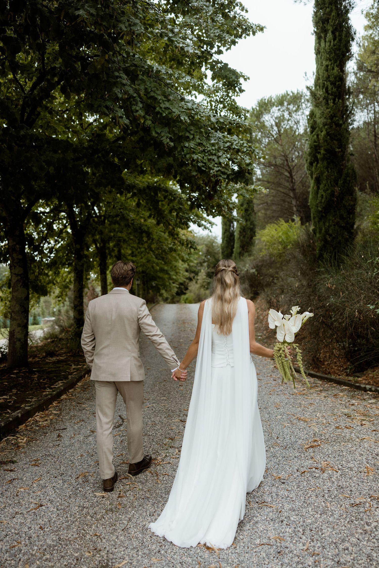 A couple in wedding attire walks away down a tree-lined gravel path in a romantic sequence of photos.