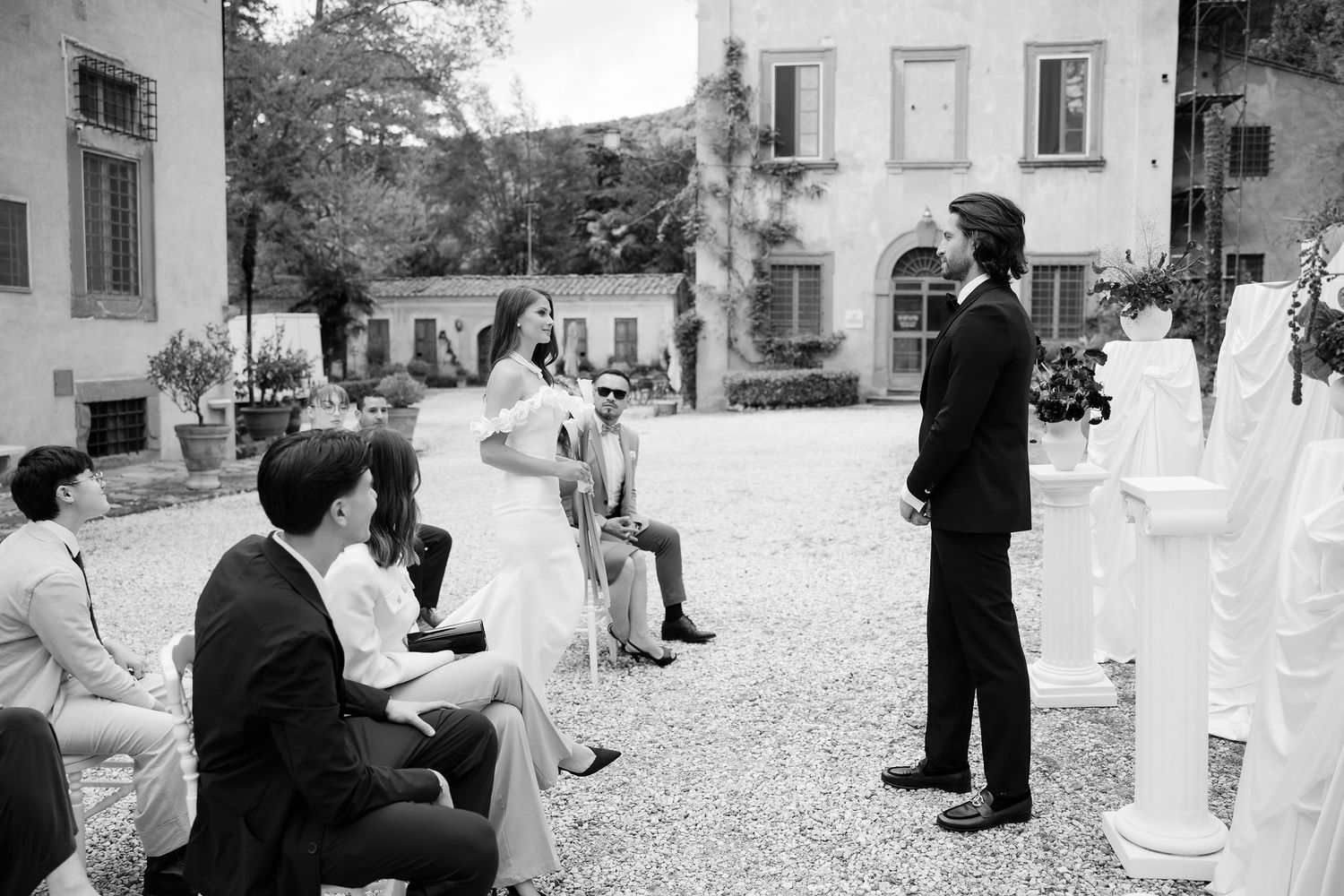 A black and white panoramic sequence of candid moments at an outdoor event with guests mingling and socializing.