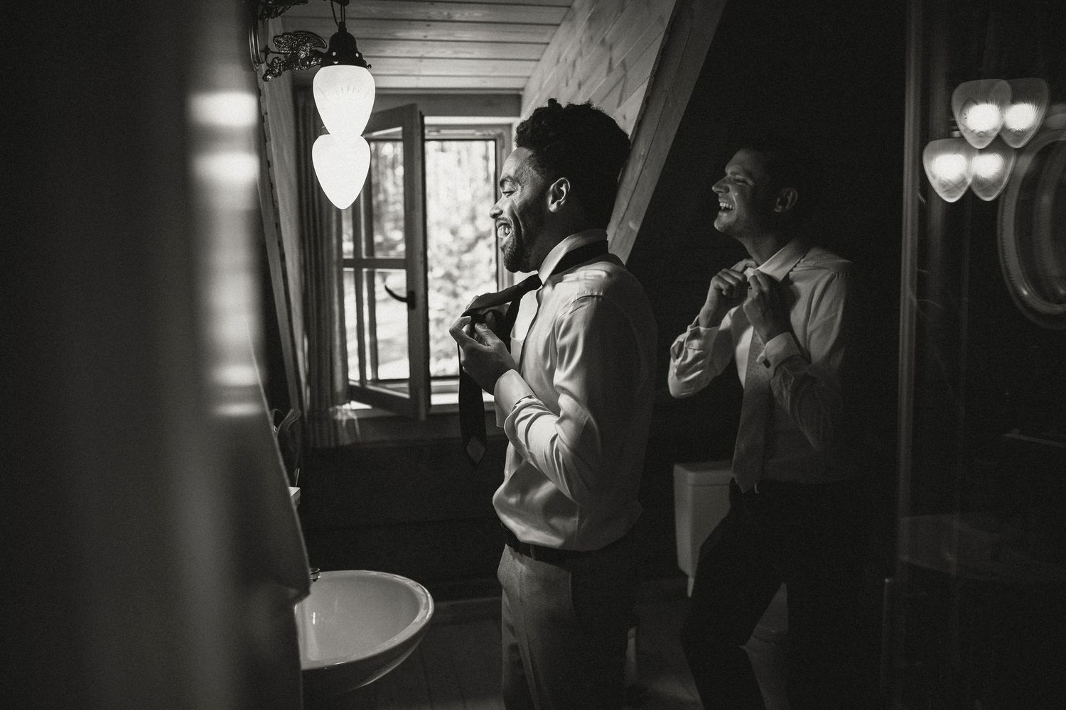 Wedding party members adjusting ties in front of bathroom mirror.