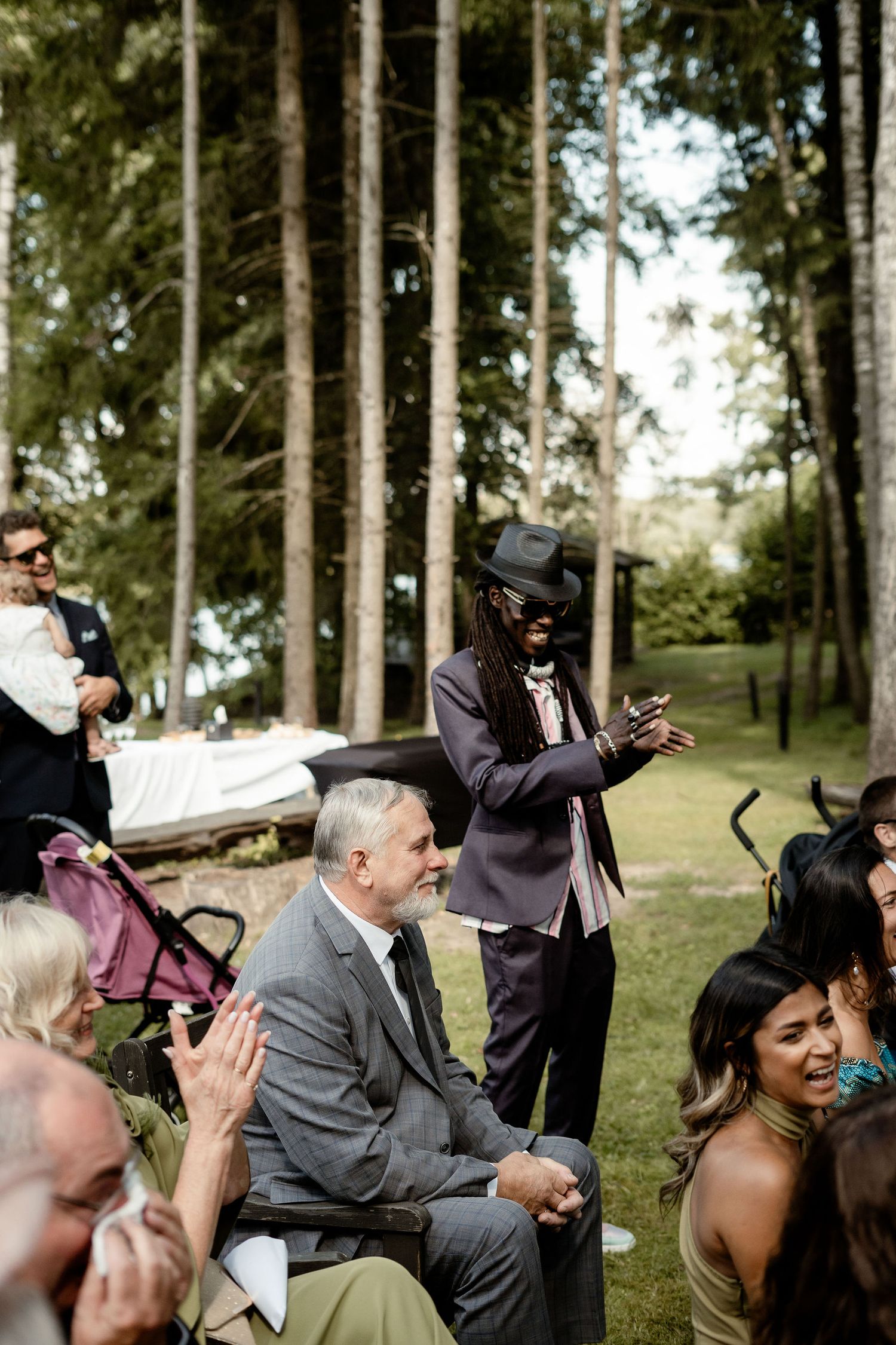 Wedding guests seated outdoors among tall pine trees during ceremony.