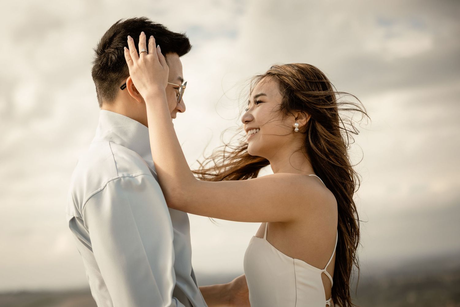 Joyful couple sharing intimate moment with wind-blown hair against cloudy sky.