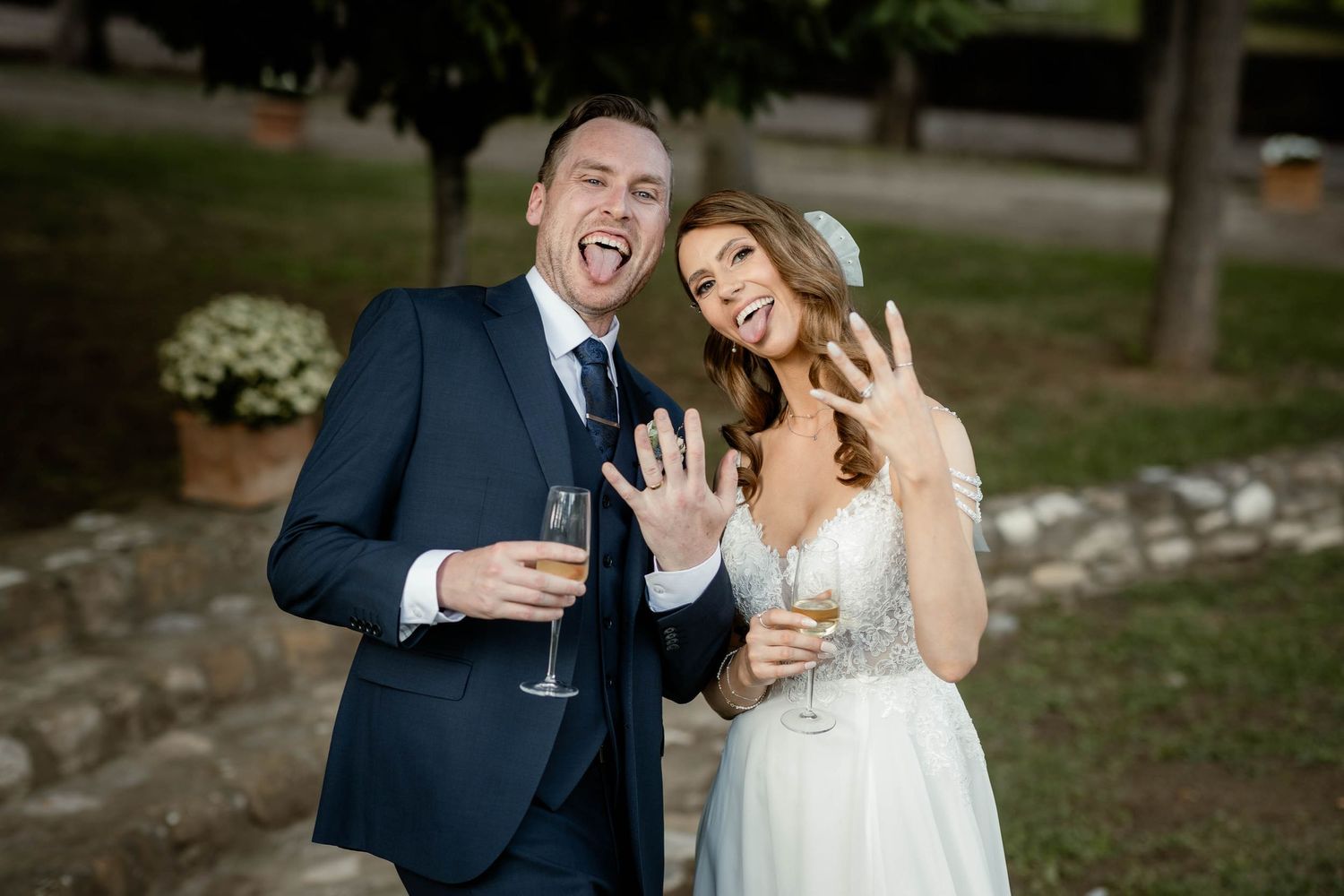 Joyful newlyweds laughing and celebrating with champagne glasses outdoors.