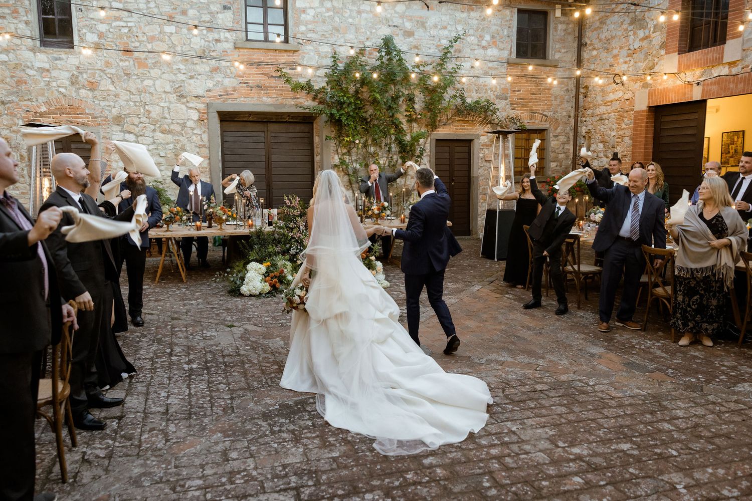 Romantic wedding dance sequence on rustic stone courtyard with guests watching during outdoor evening reception.