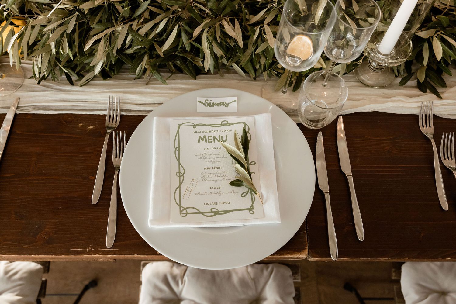 Wedding reception table settings with elegant white plates, wine glasses, and eucalyptus garland decorations.