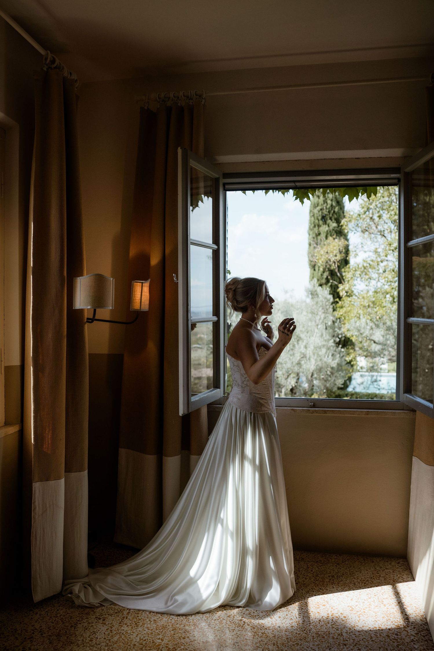 A bride in a flowing white gown stands silhouetted against sunlit windows in a series of elegant indoor photos.