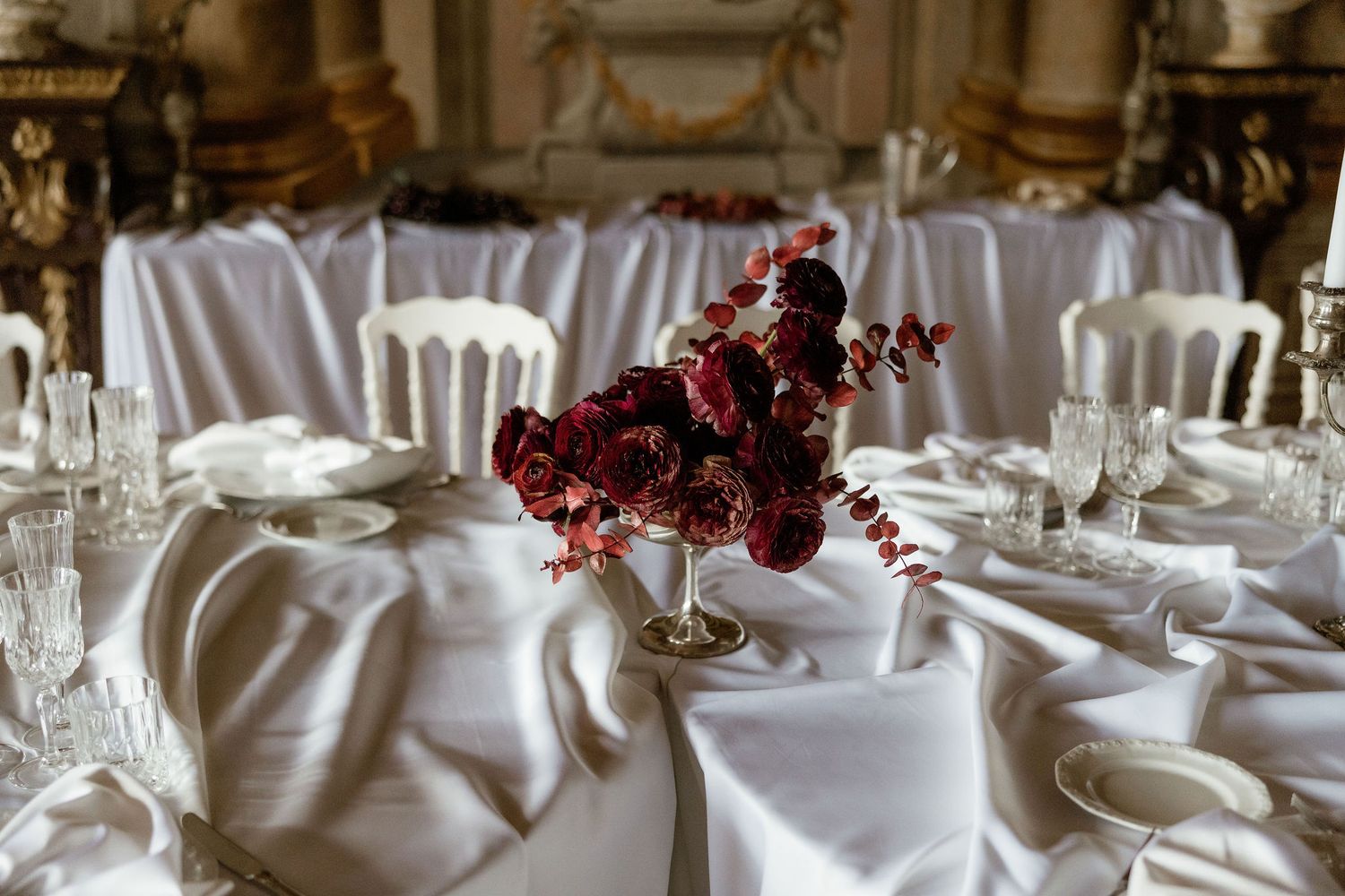 Elegant wedding table setting with dark red floral centerpiece and crisp white linens at formal reception venue.