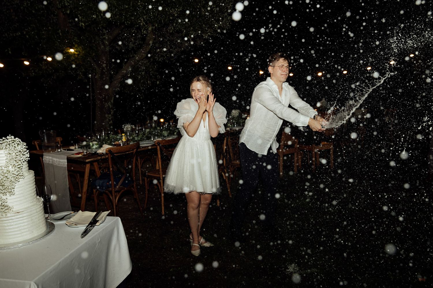 A celebratory moment at a wedding reception with champagne popping and snow-like effect in the air.