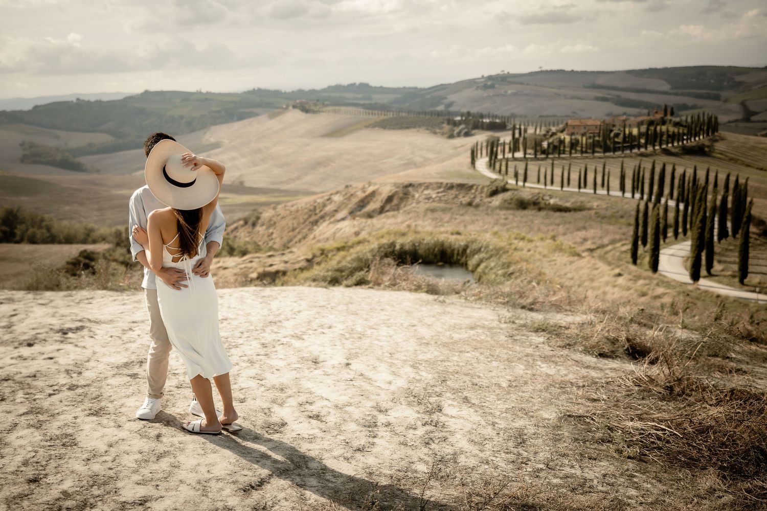Romantic couple embracing while overlooking the iconic winding cypress tree road in Tuscany.