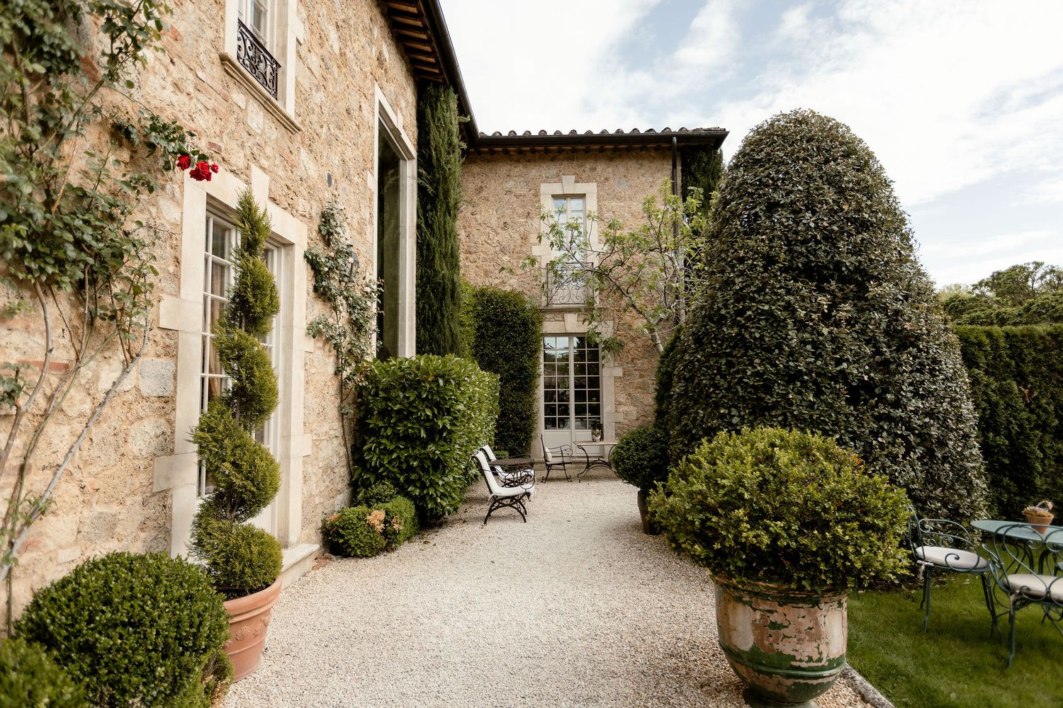 A charming courtyard with stone walls, potted plants, and manicured topiaries at an elegant Tuscan villa.