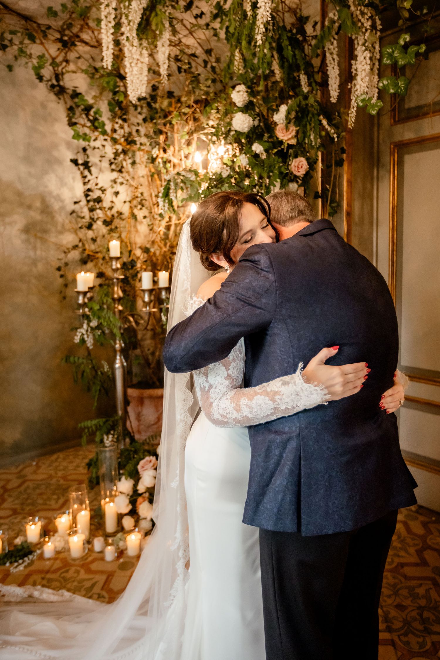 A wedding couple dancing intimately in a romantic setting with floral decorations and candlelight.