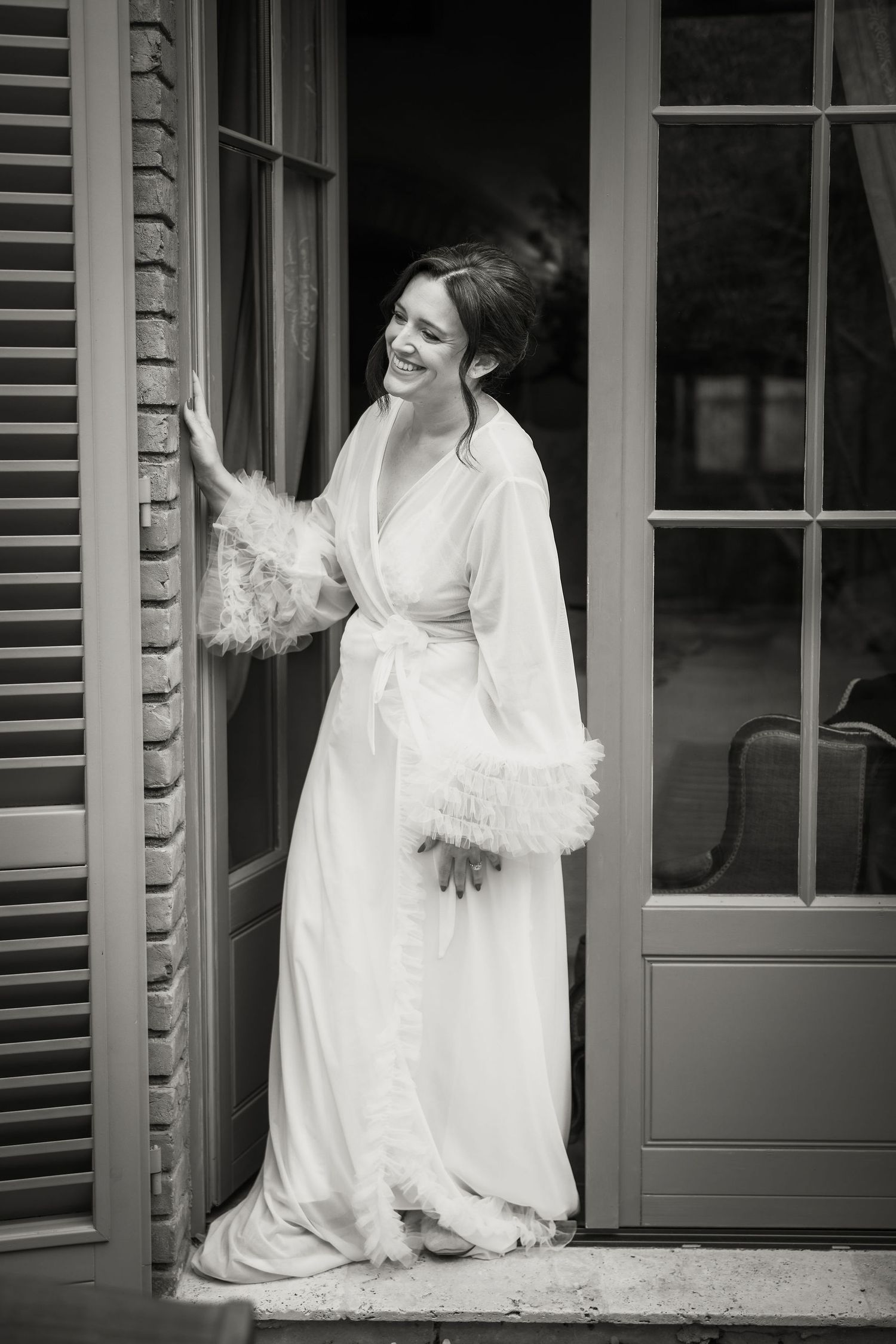 Black and white photo of a person in an elegant white robe with fur trim standing in a doorway.