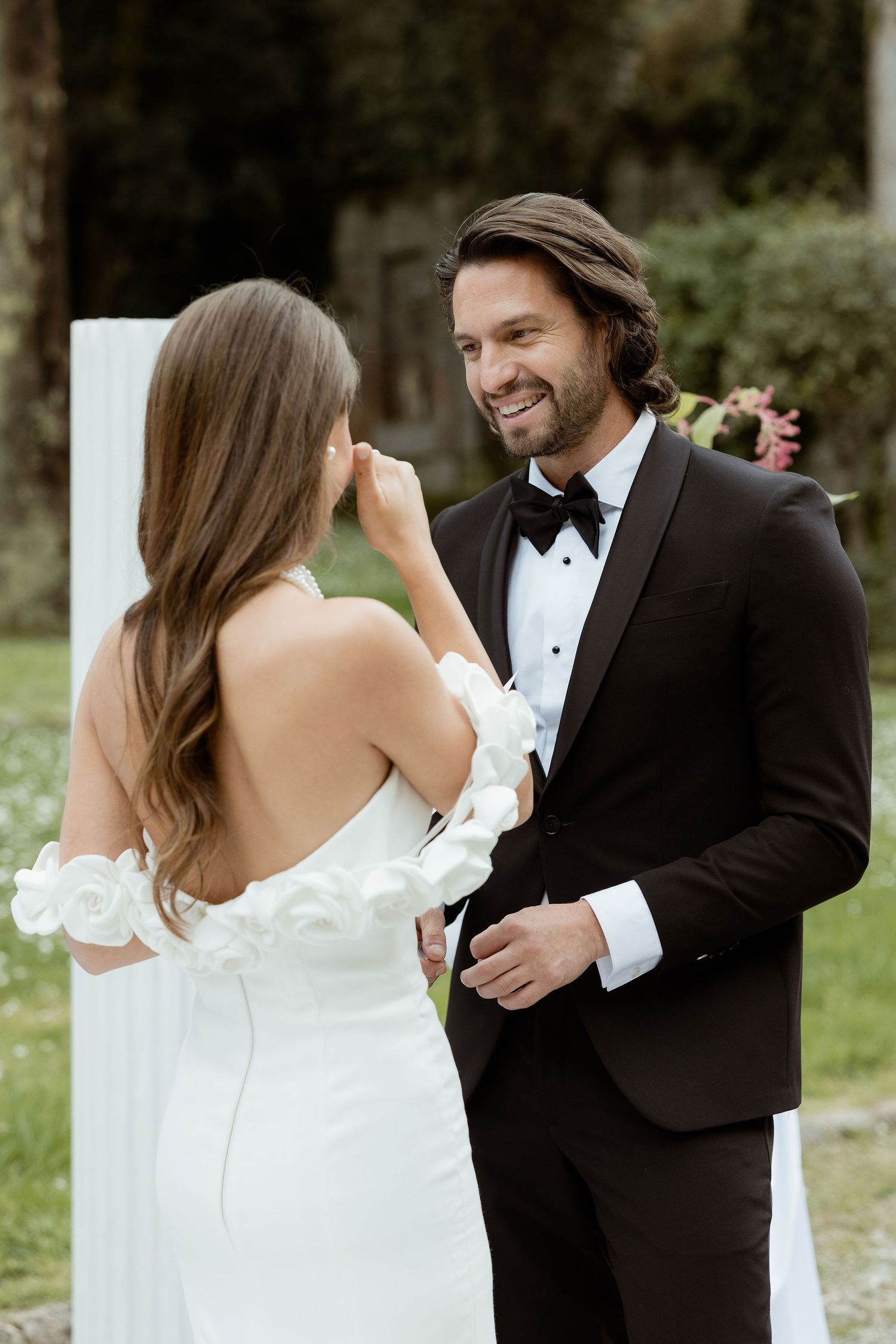 A couple shares a candid moment during their wedding photoshoot, with the bride in white and groom in a black tuxedo.