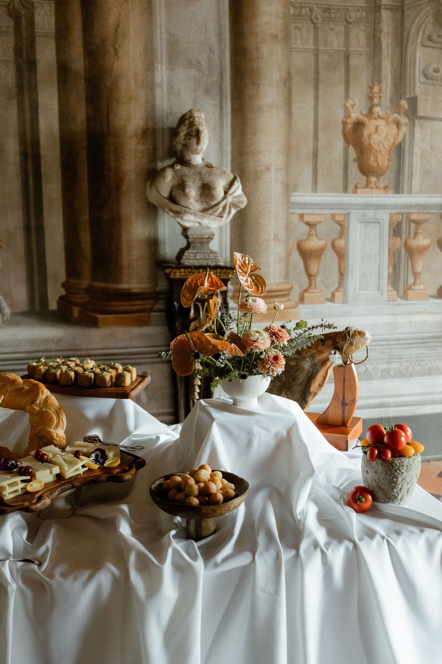 Elegant buffet table with pastries and fruit set against classical interior with marble bust and columns.