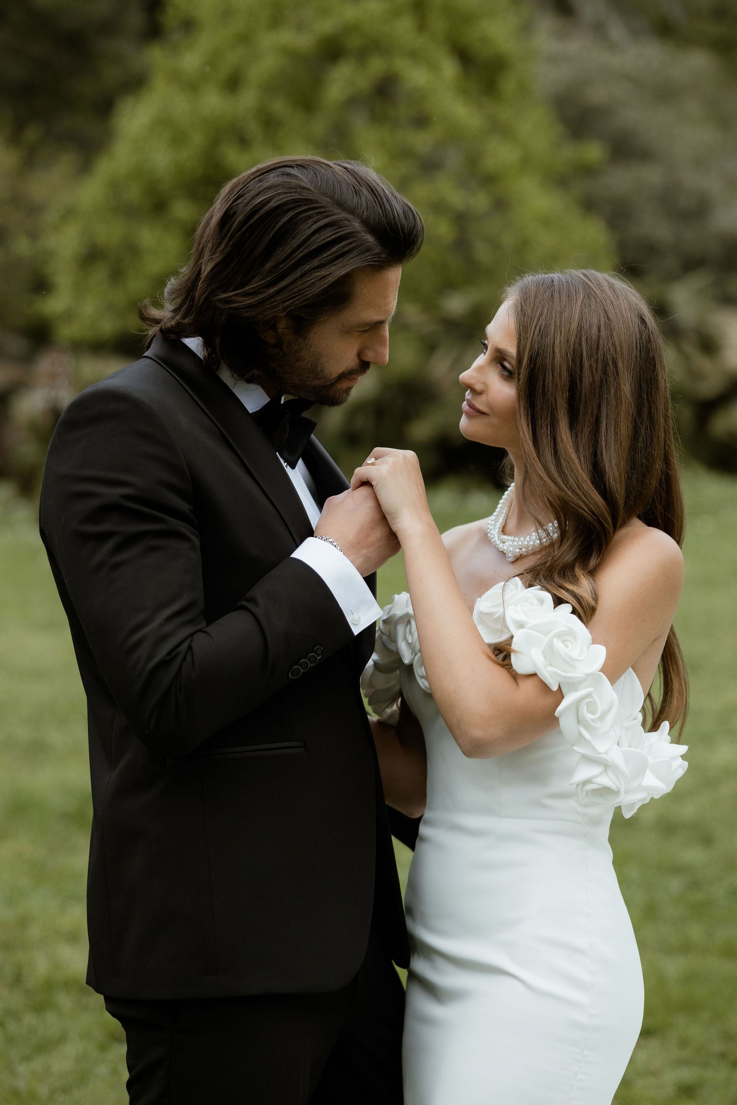 Elegant couple shares romantic moment in formal wedding attire outdoors with groom kissing bride's hand.