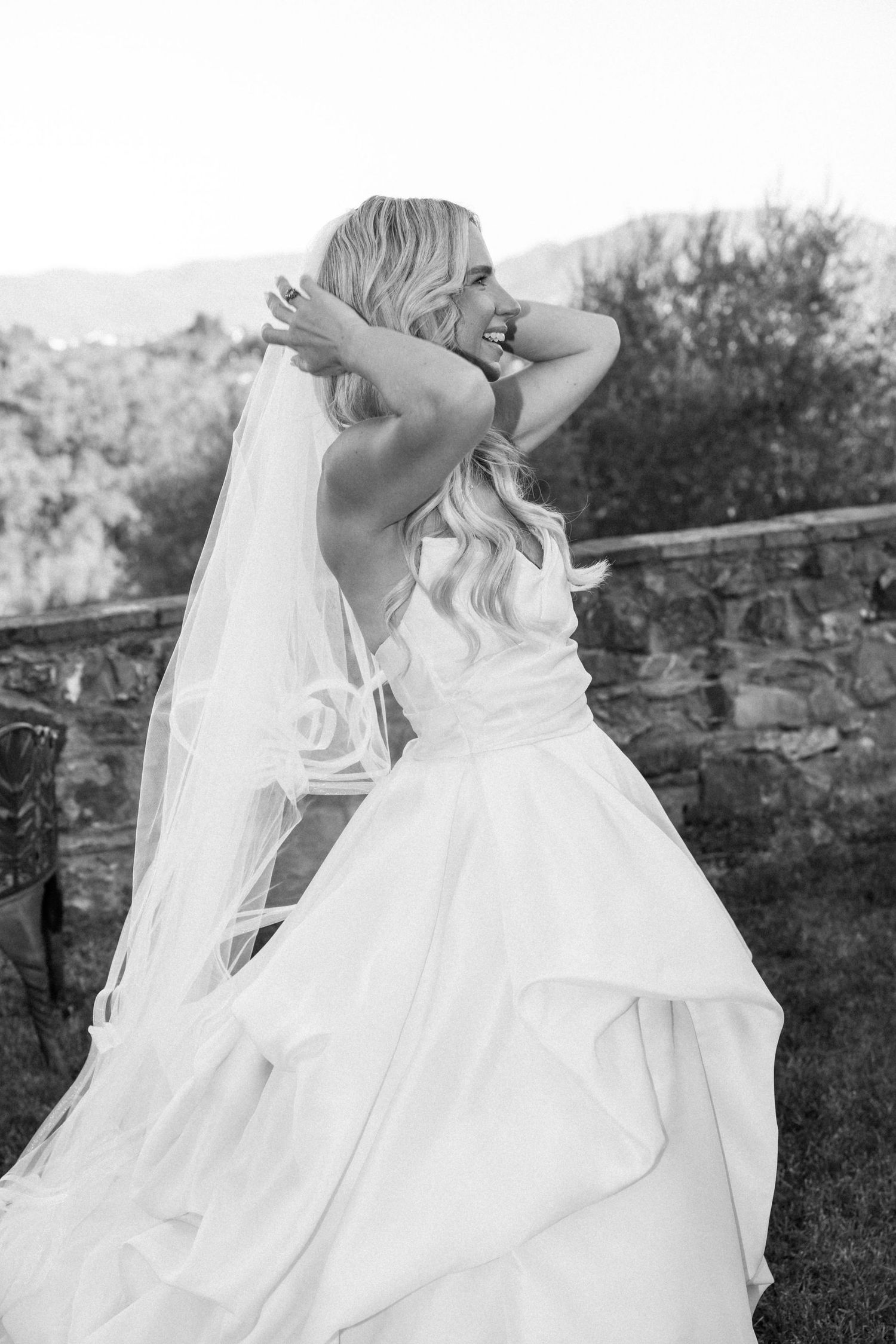 A bride's white dress with layers of tulle and ruffles flows gracefully in an outdoor garden setting.