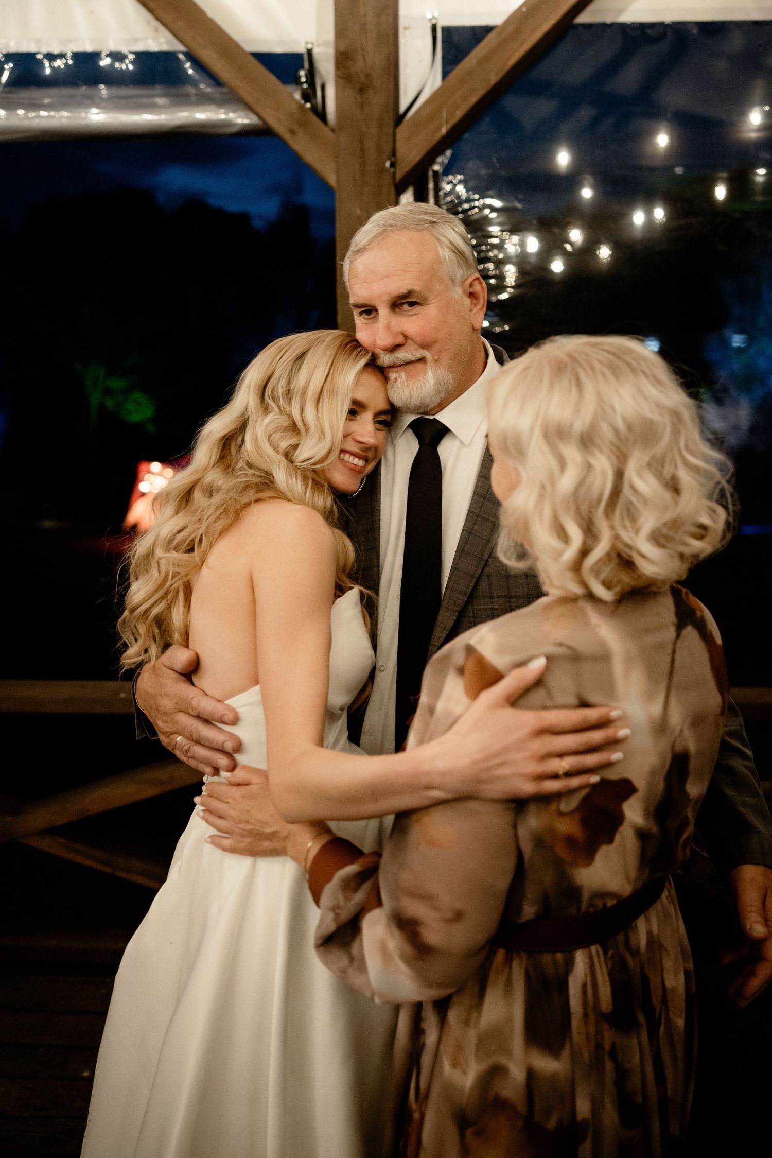 A tender emotional moment between loved ones embracing during a wedding reception with string lights in the background.
