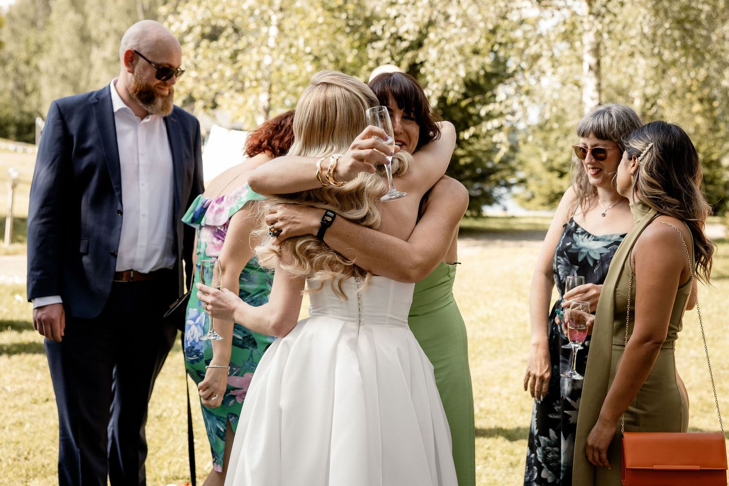 Emotional group hug during outdoor summer wedding celebration.
