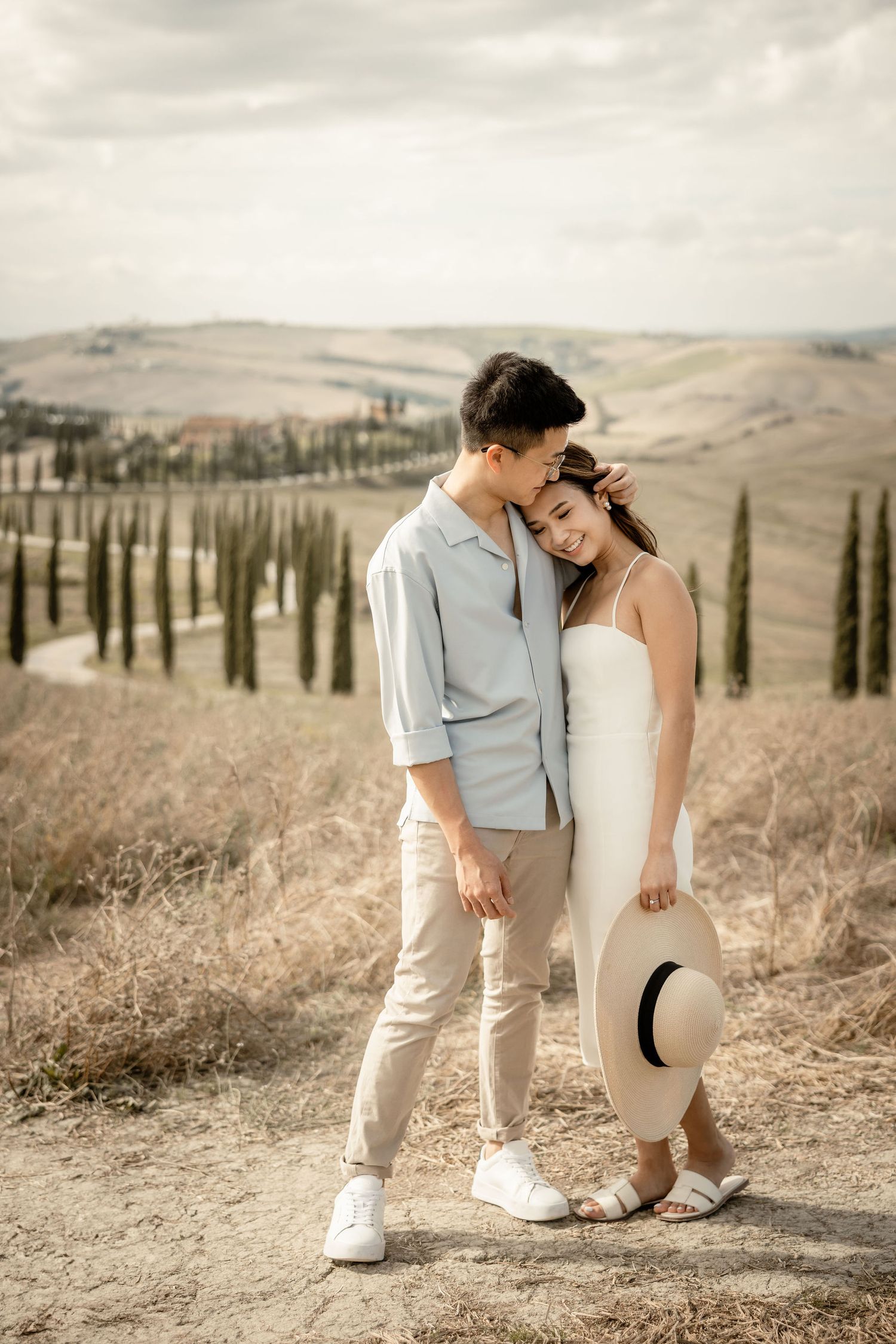 Couple sharing tender moment on hilltop with Tuscan cypress landscape.
