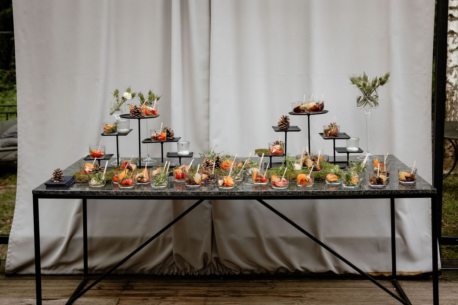 Multi-tiered appetizer display featuring various hors d'oeuvres on black stands against white backdrop.