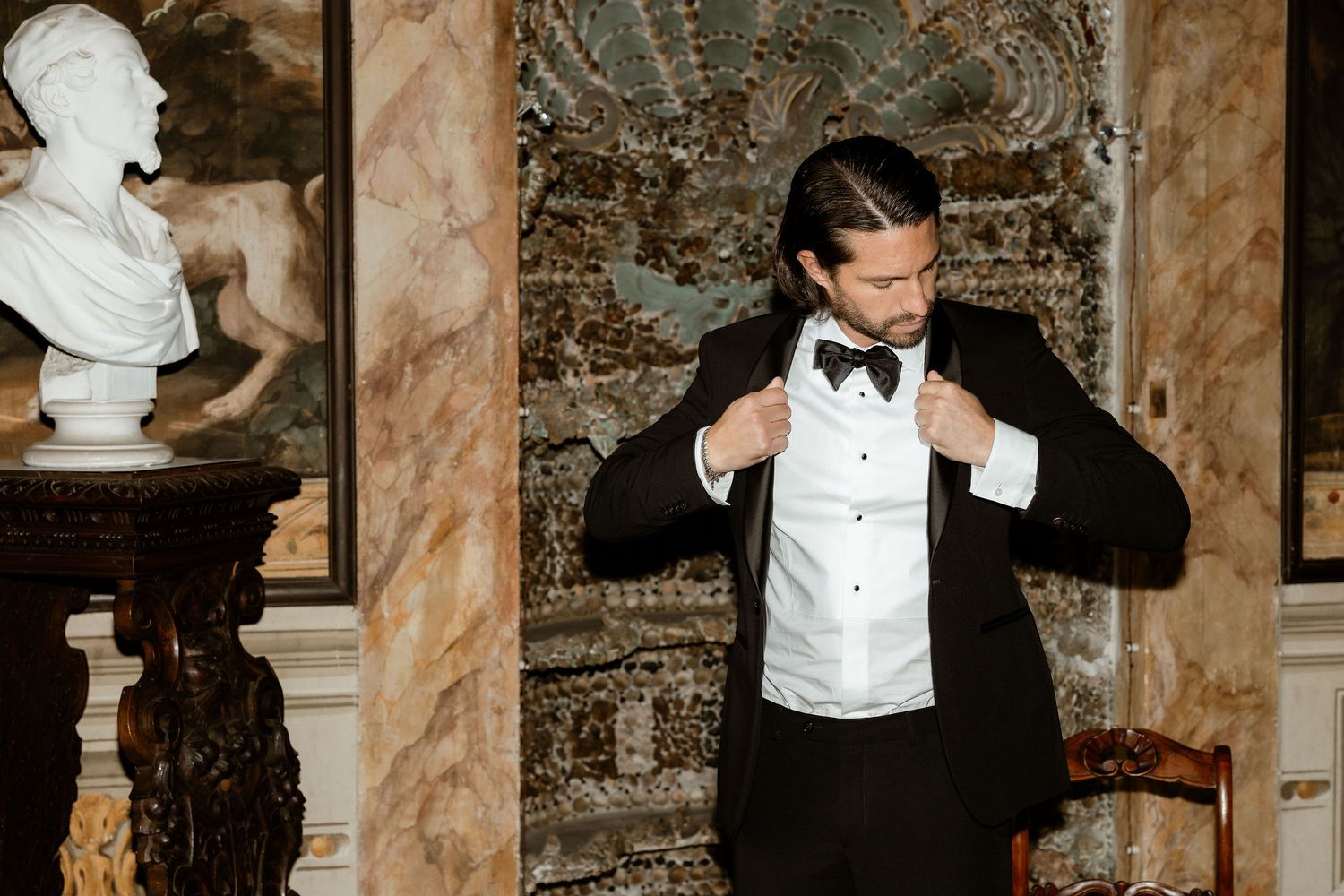 A sequence of formal portraits showing someone adjusting their bowtie while standing next to a marble bust in an ornate room.