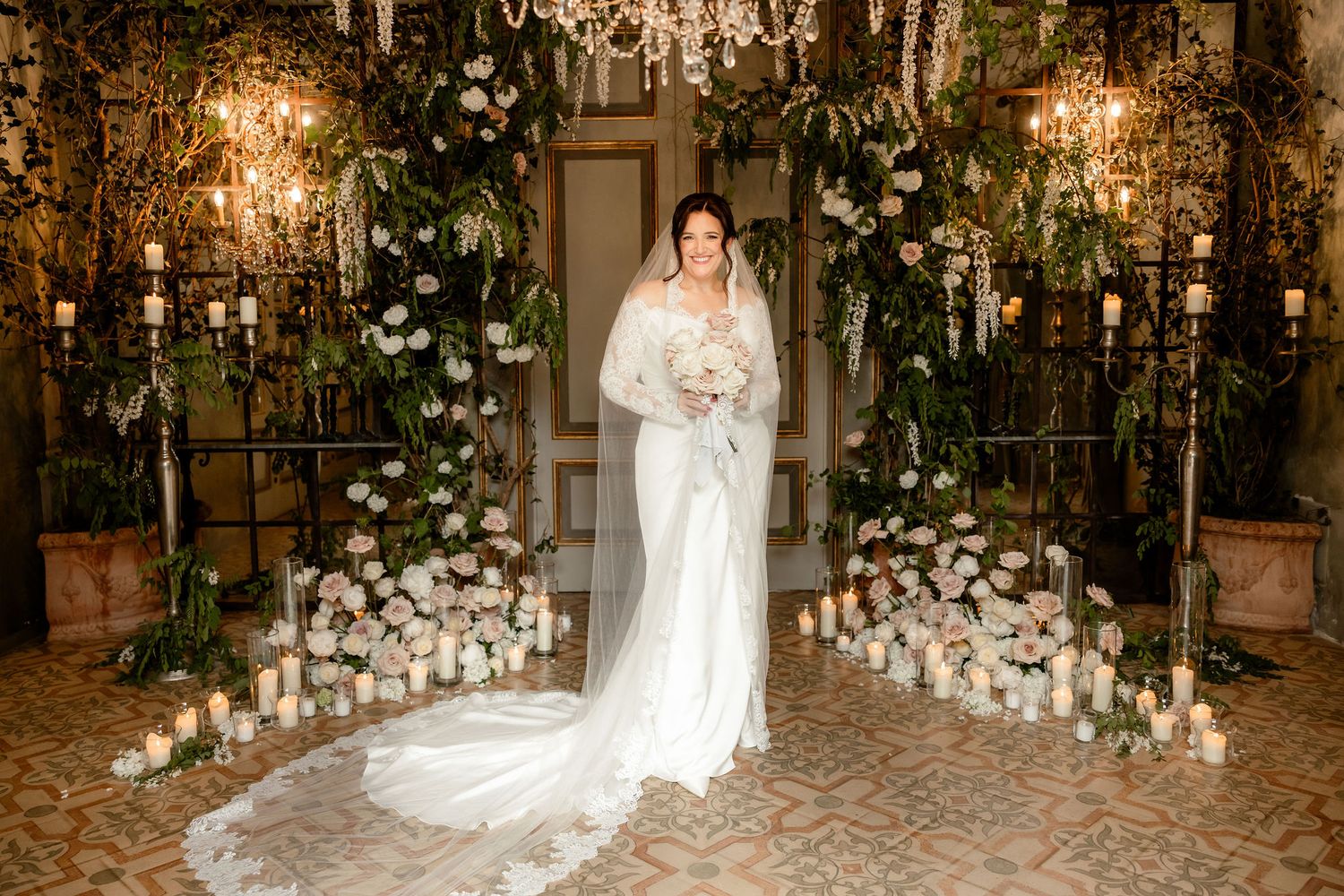 Elegant indoor wedding scene with floral arch, glowing candles, and ornate chandeliers creating a romantic ambiance.