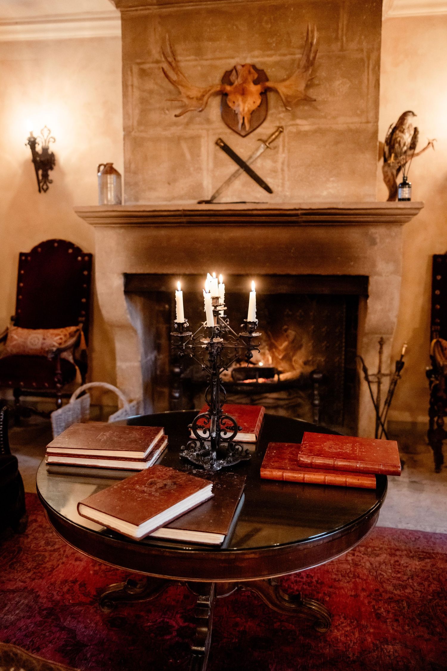 Cozy library setting with antique books, candelabra and moose antlers over stone fireplace on red oriental rug.