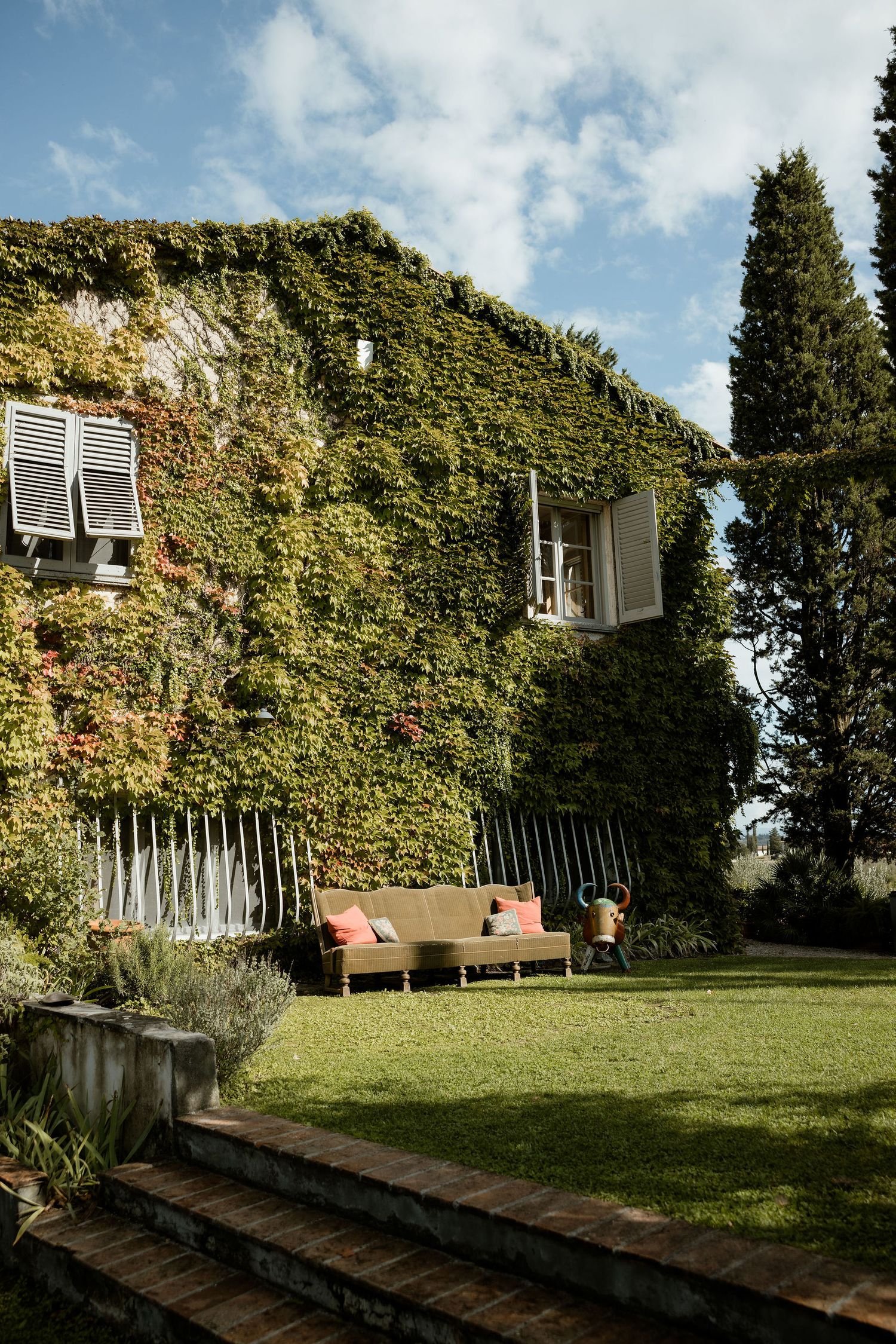 Ivy-covered building wall with air conditioning units and benches along a grassy pathway on a sunny day.