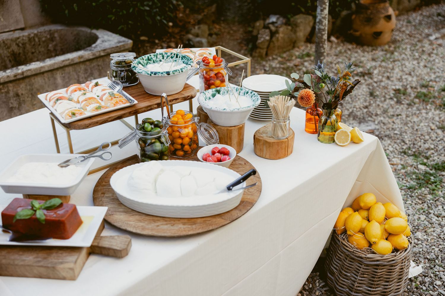 Rustic outdoor table setting with citrus fruits, wooden boards, and white ceramic plates on a textured surface.