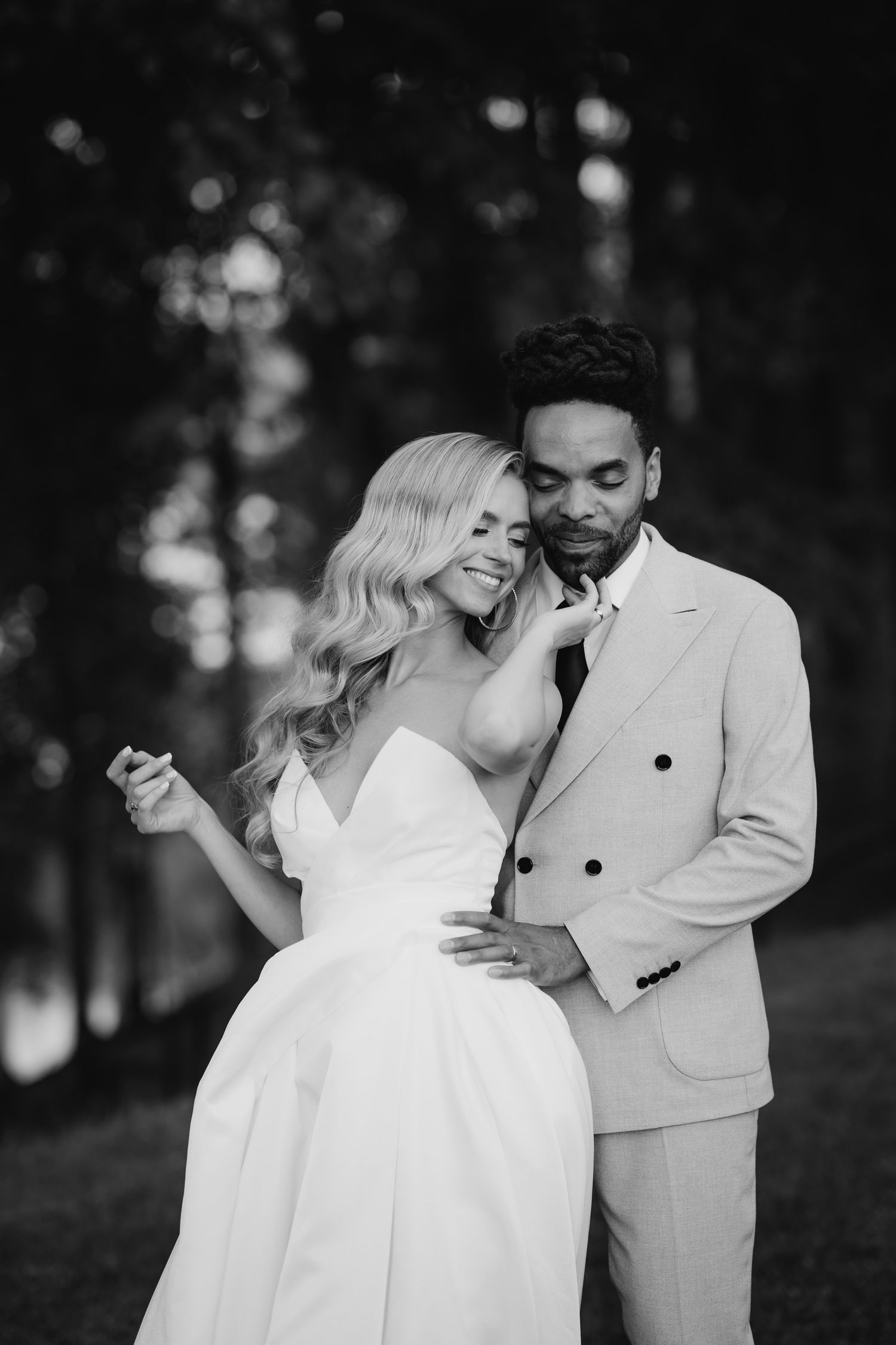 A romantic black and white wedding photo of a couple in light colored attire sharing an intimate moment outdoors.