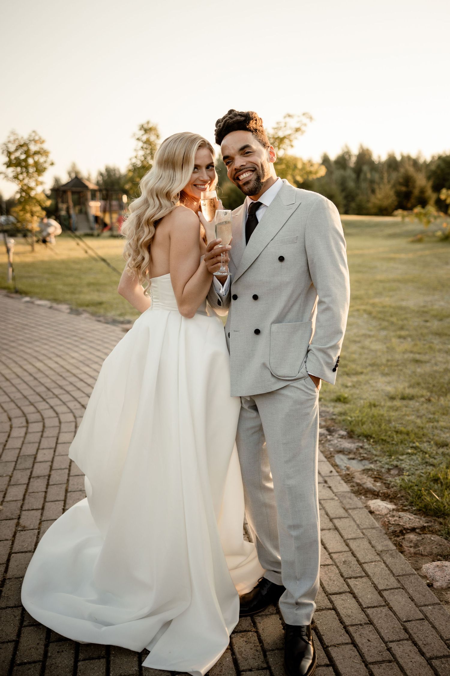A romantic wedding photo of a couple laughing together on a brick path at sunset while wearing elegant white attire.