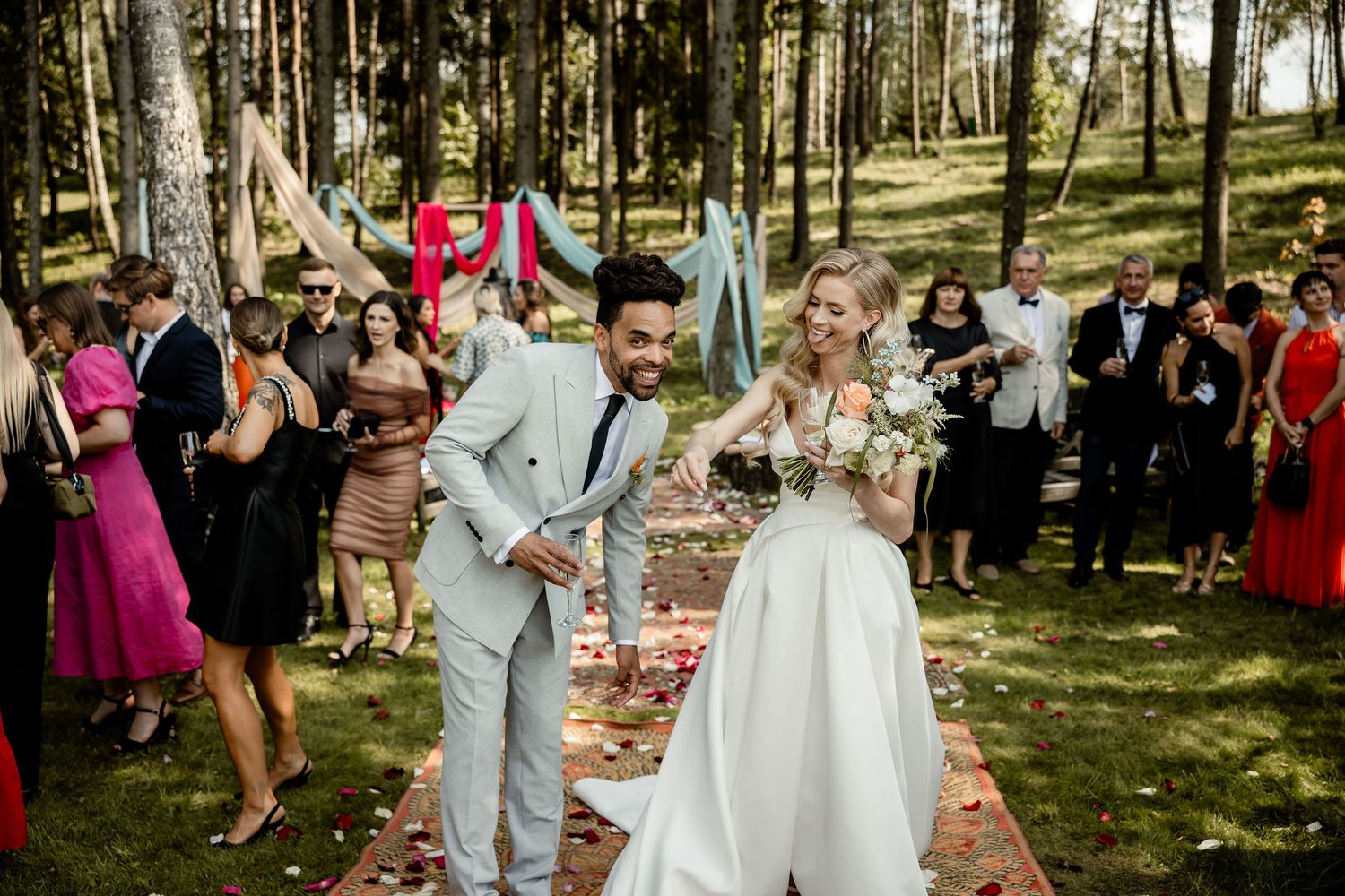 Joyful outdoor wedding ceremony in a wooded setting with guests watching the celebration.