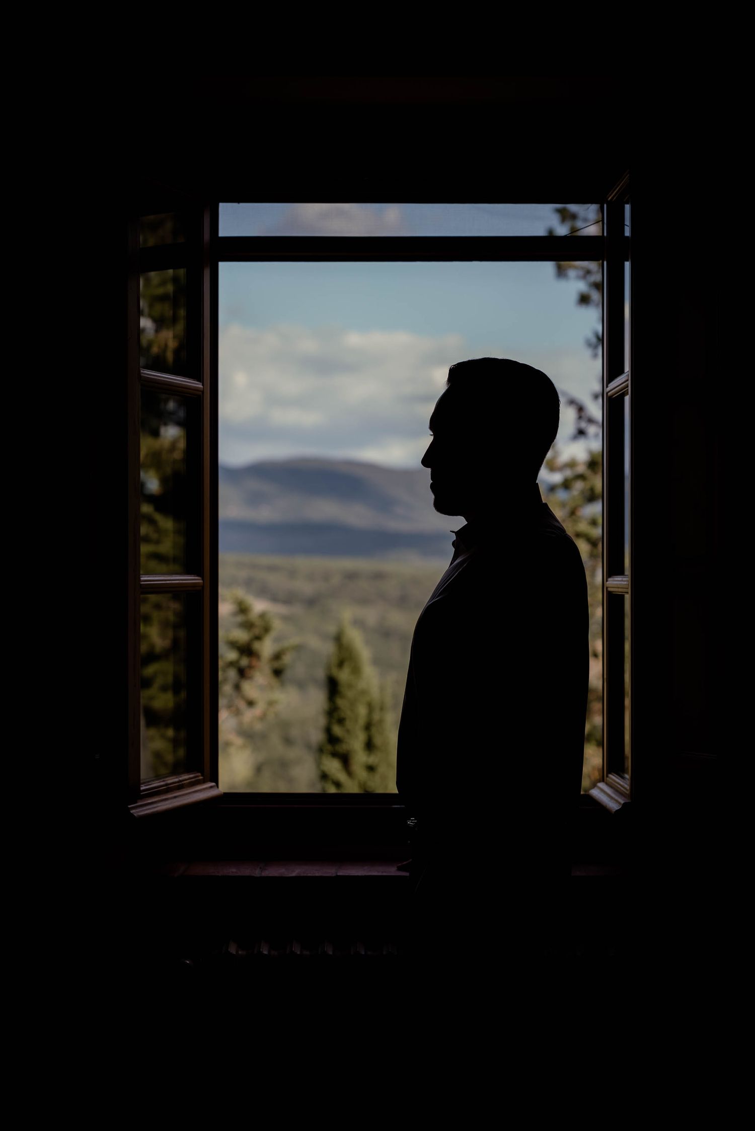 Silhouette framed in window overlooking mountainous landscape at dusk.