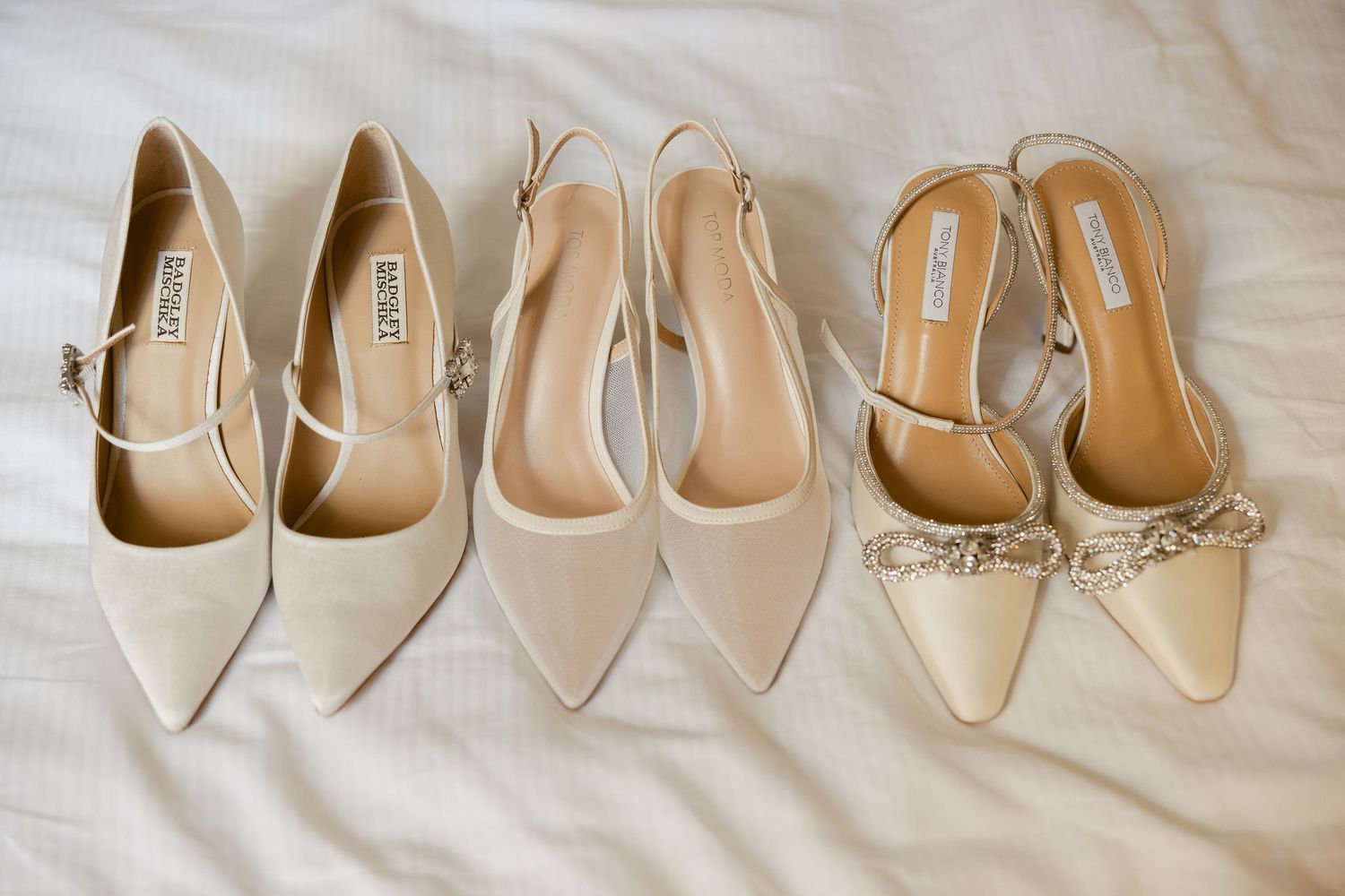 Collection of elegant nude and beige women's dress shoes and pumps arranged in a row on white fabric.